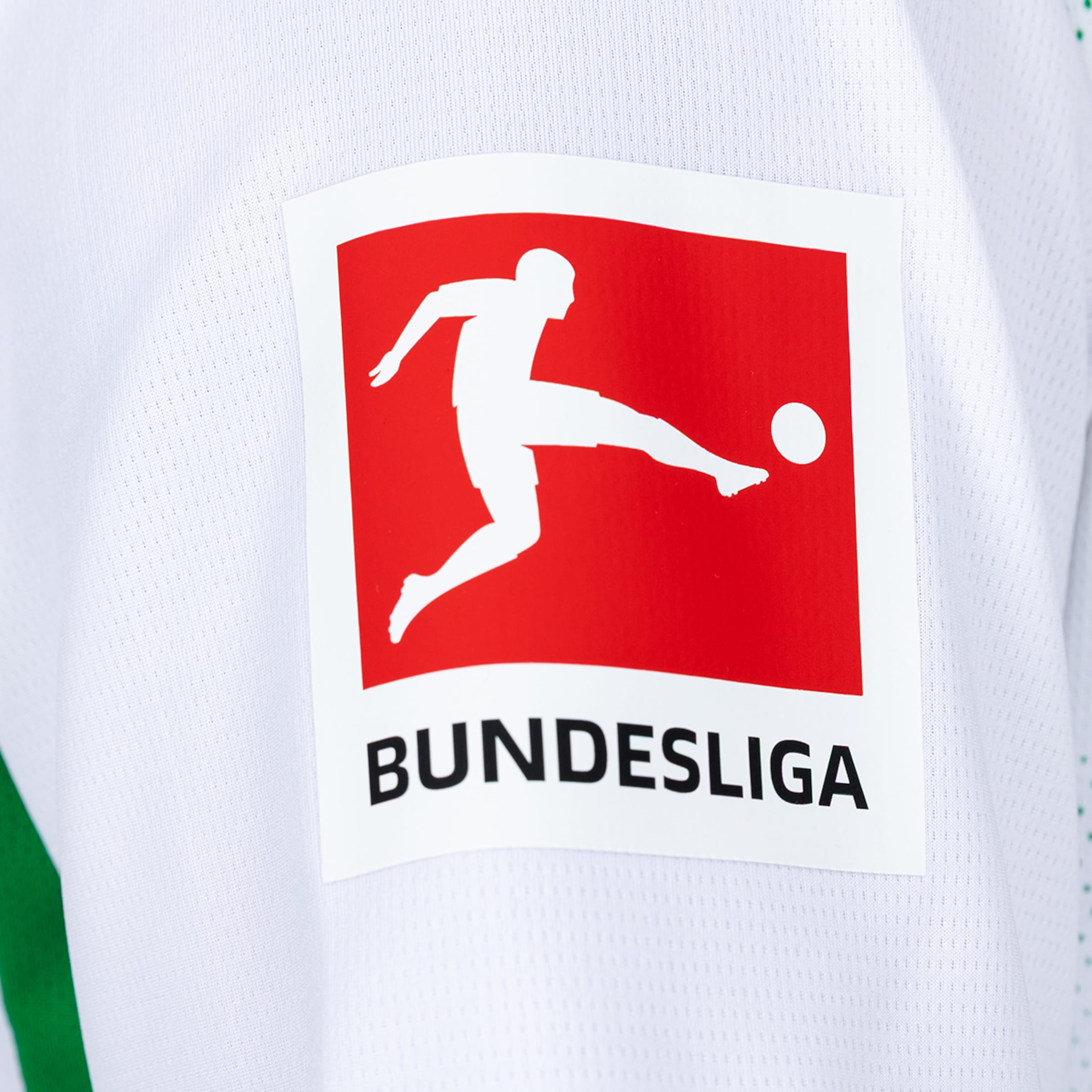 Nahaufnahme des Bundesliga-Logos auf einem weißen Trikot. Rotes Feld mit Fußballer-Silhouette und dem schwarzen Schriftzug „BUNDESLIGA“.