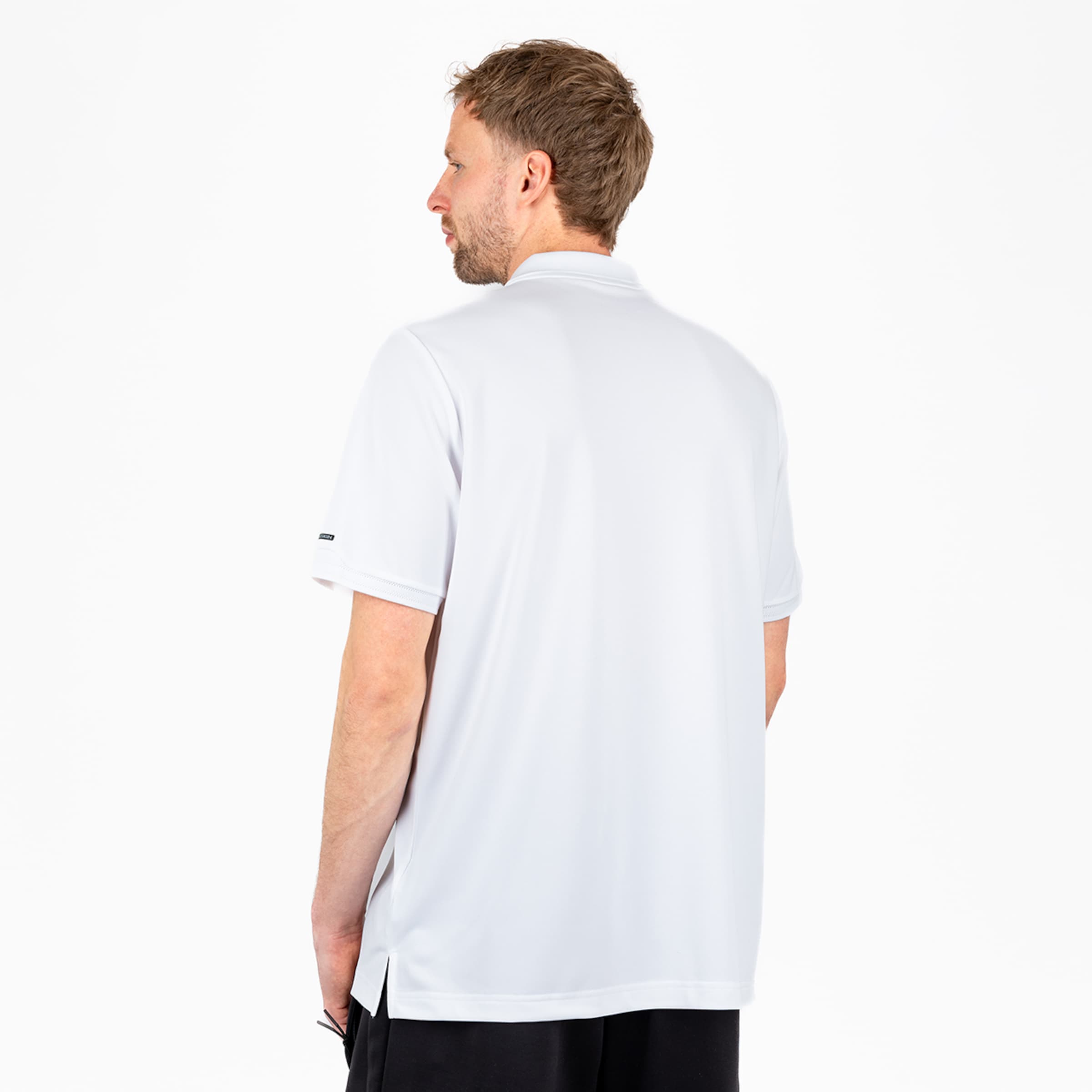 Rear view of a man wearing a white short-sleeved polo shirt and black shorts against a white background.