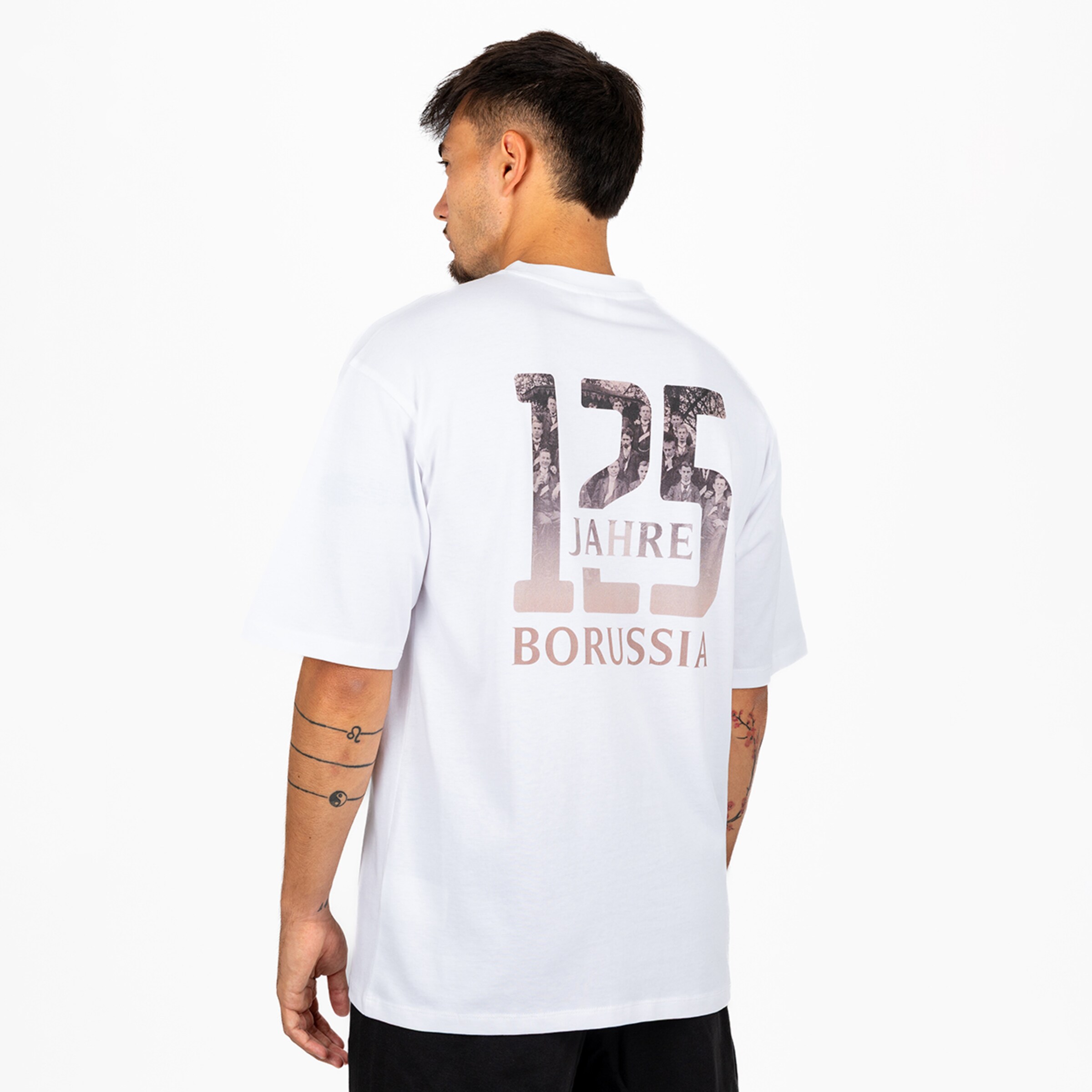 Rückansicht eines Mannes im weißen T-Shirt mit „125 JAHRE BORUSSIA“-Grafik, die ein historisches Gruppenfoto in den Zahlen zeigt.