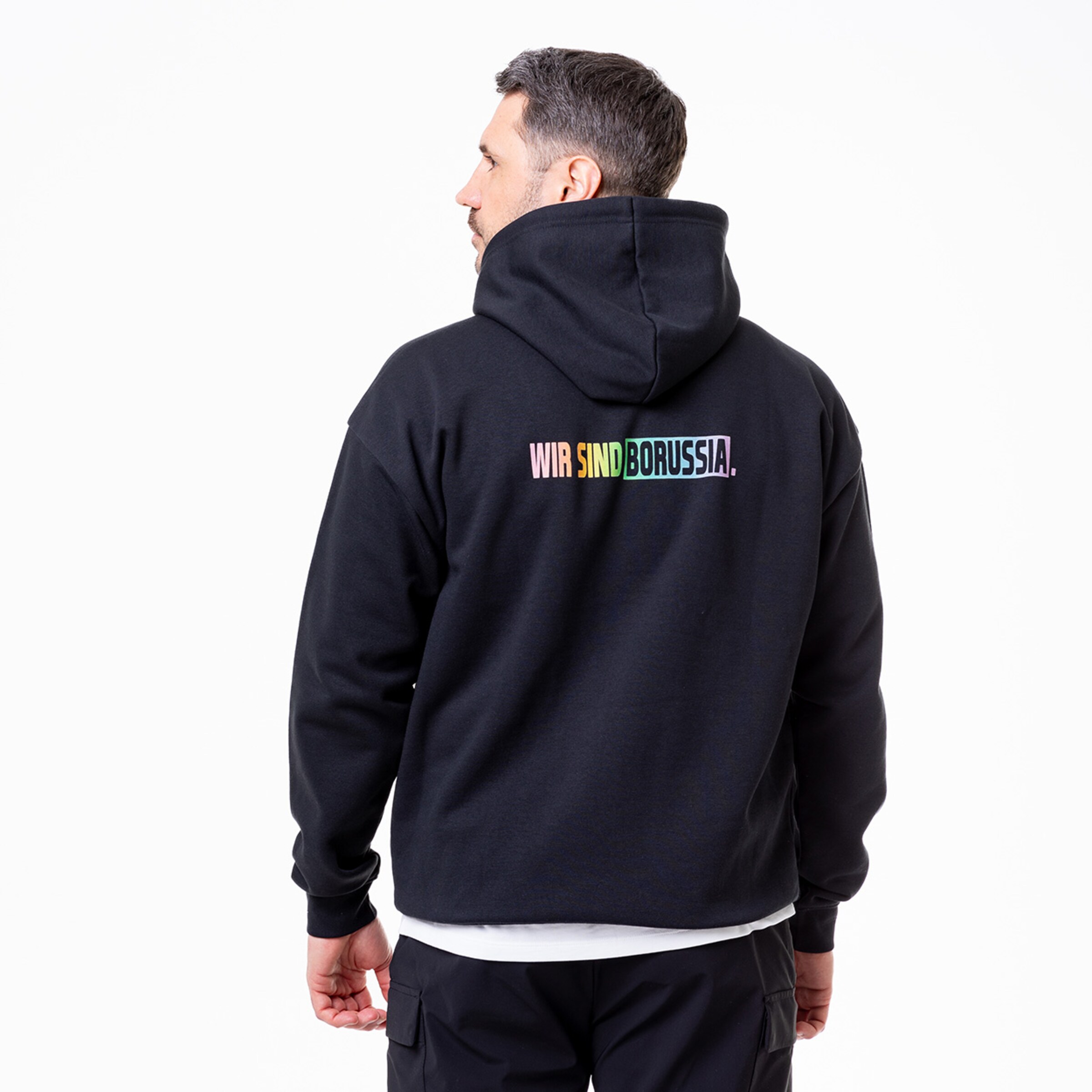 Mann zeigt den Rücken eines schwarzen Hoodies mit buntem Schriftzug WIR SIND BORUSSIA.
