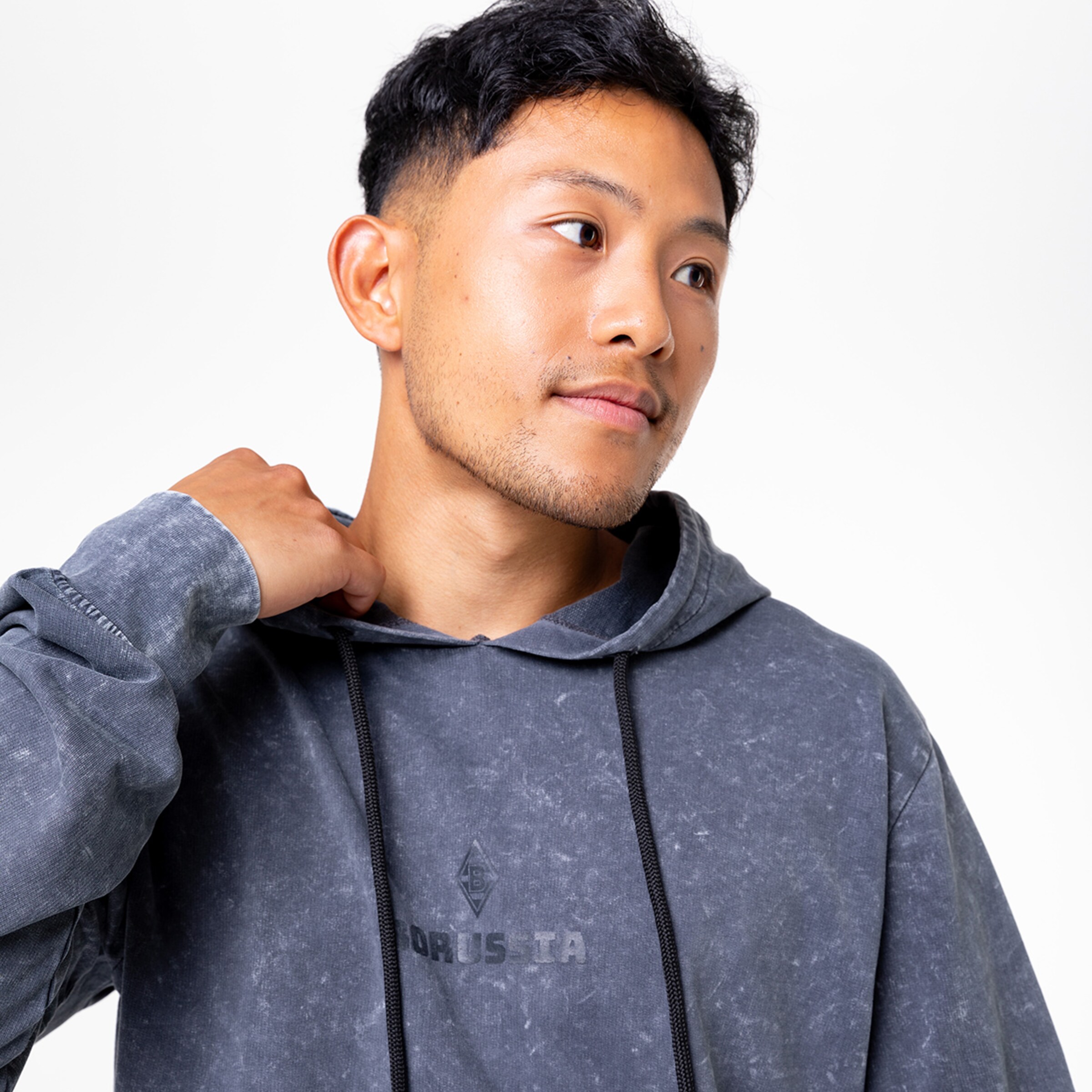 Ein junger Mann trägt einen grauen Hoodie mit einer Kapuze und schaut nachdenklich.