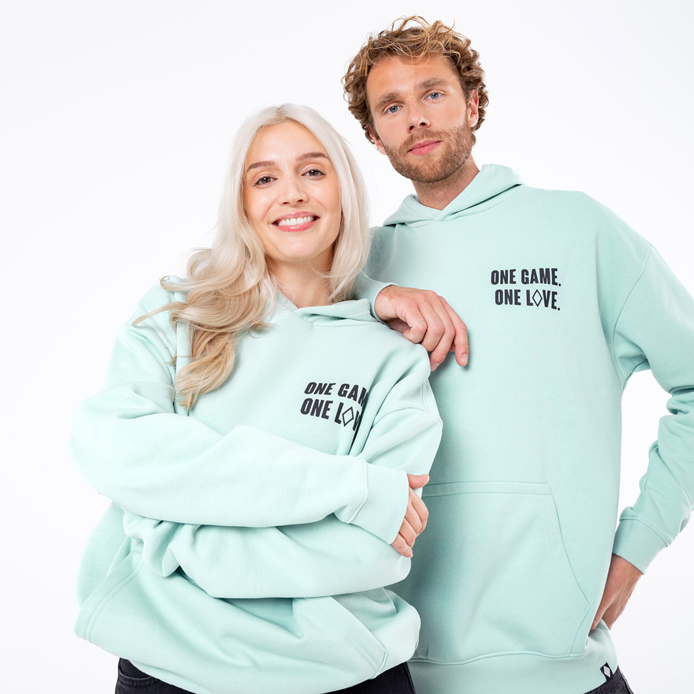 Ein Mann und eine Frau tragen mintfarbene Kapuzenpullover mit dem Text ONE GAME. ONE LOVE.
