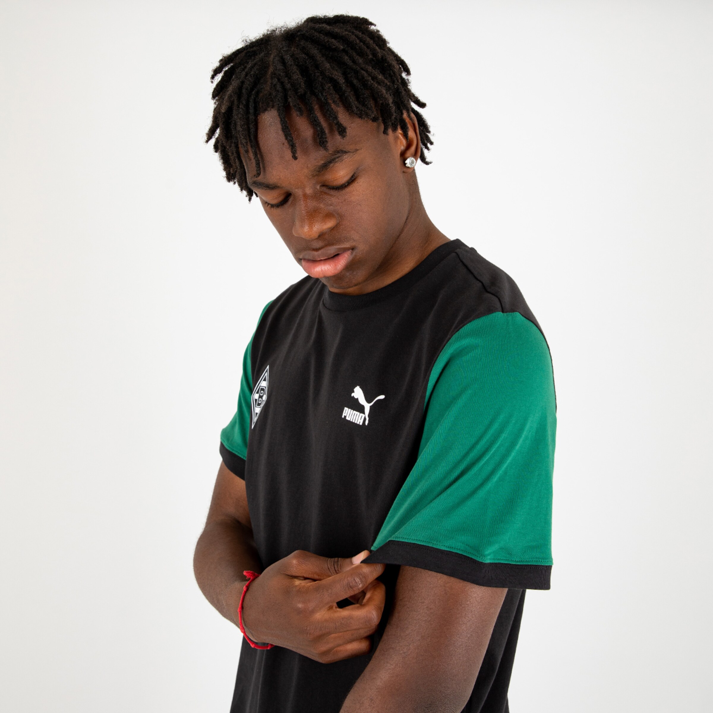 A young man with black curly hair wears a black shirt with green sleeves and touches the sleeve.