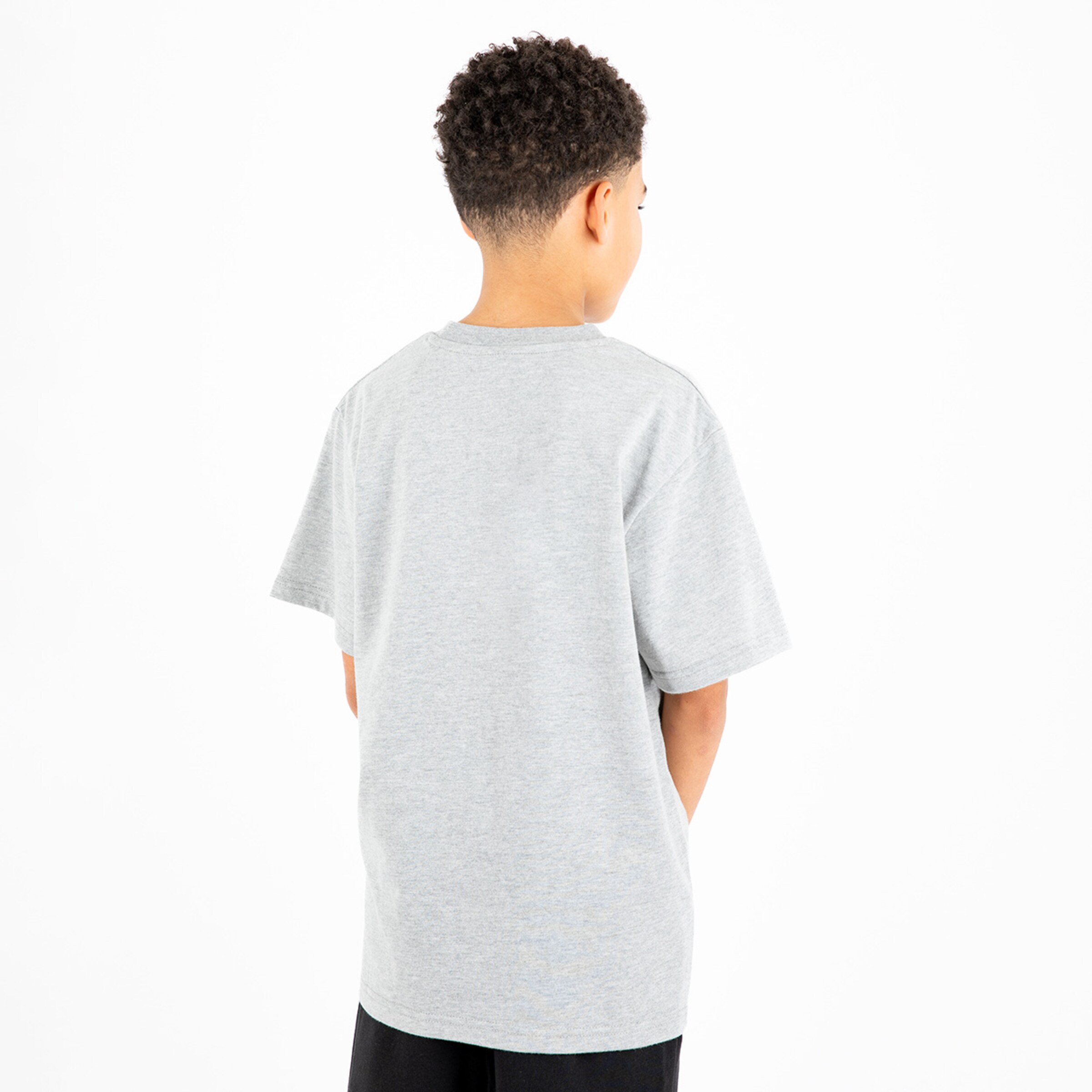 Junge steht mit den Händen in den Taschen trägt ein graues T-Shirt von hinten.