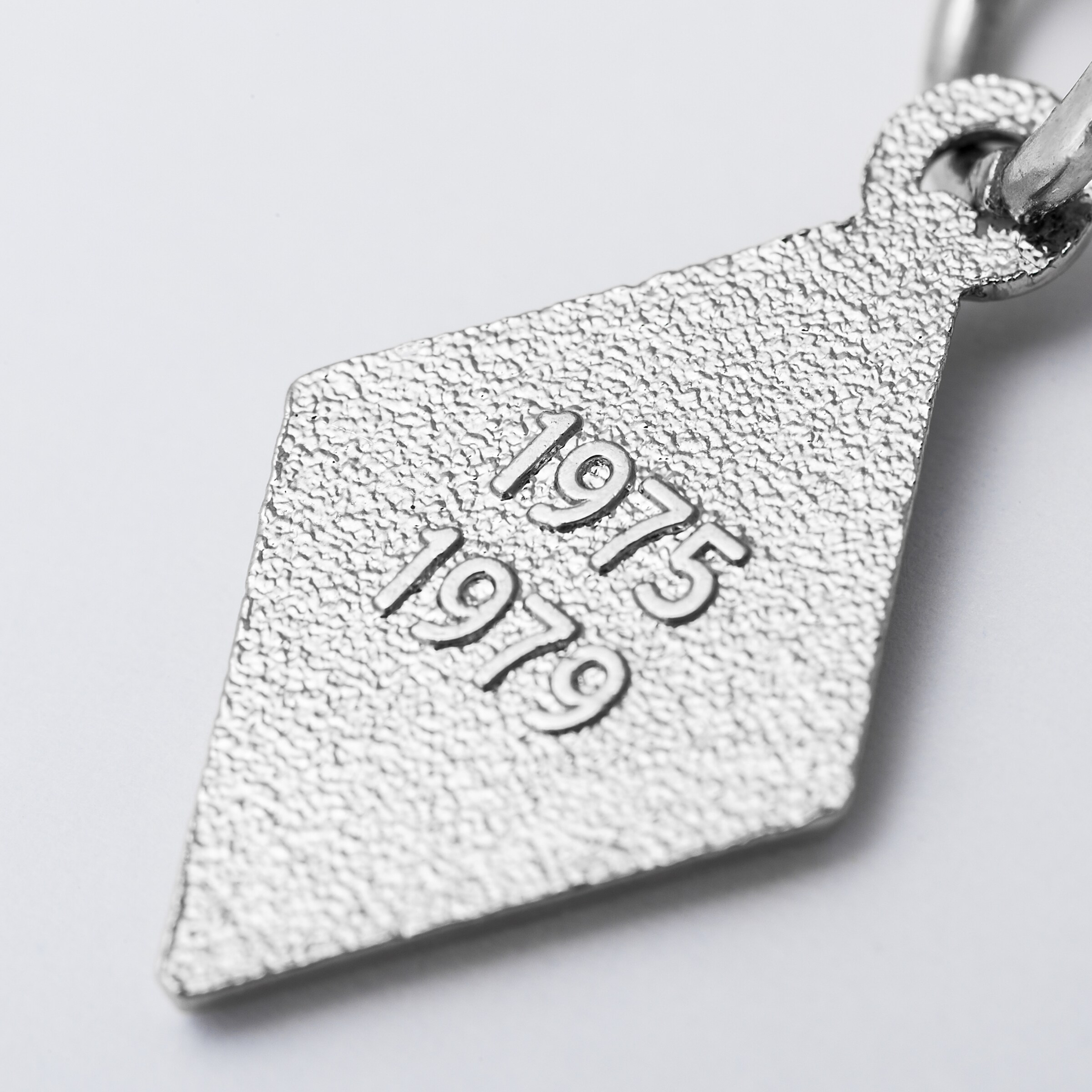 Silver diamond-shaped pendant engraved with the years 1975 and 1979.