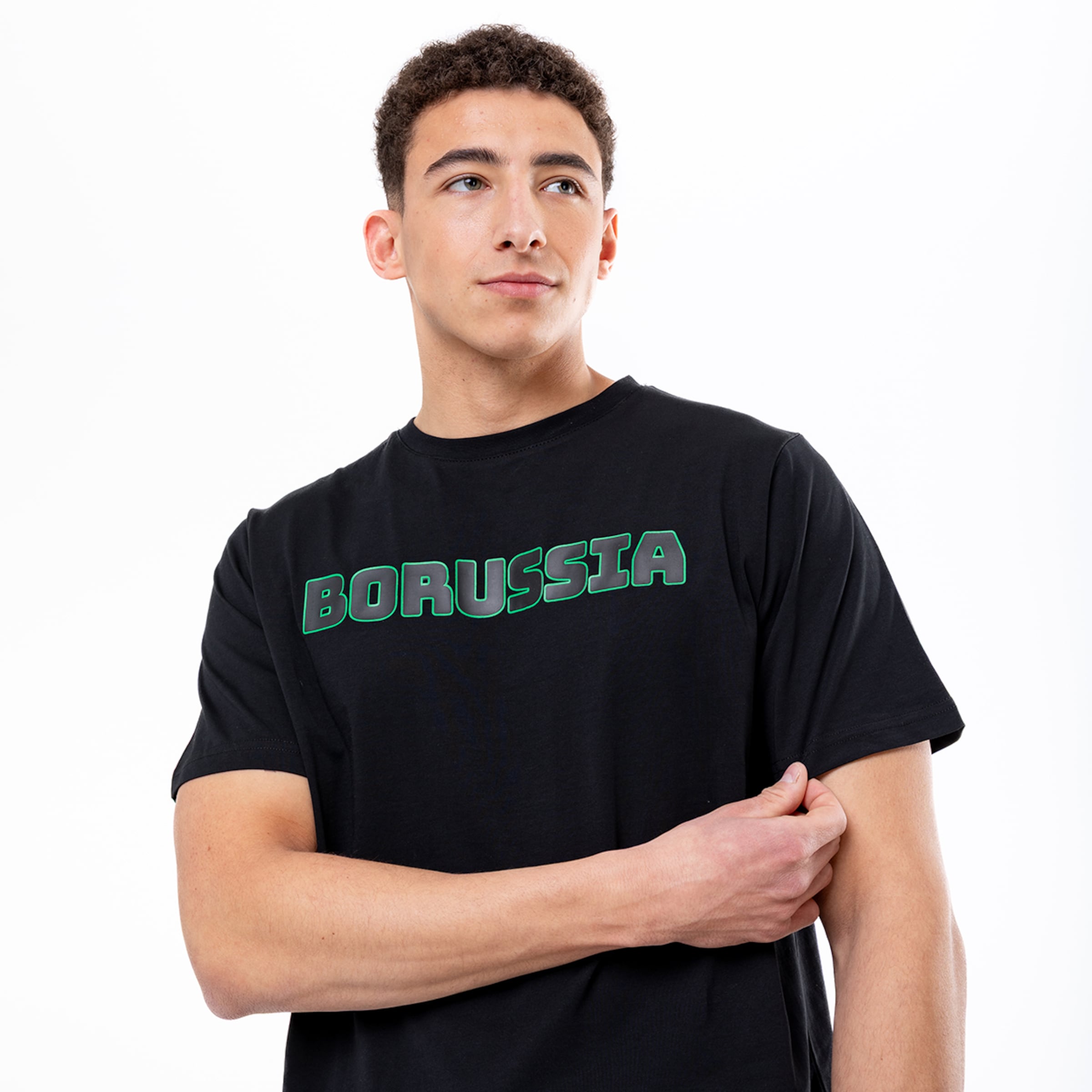 Junger Mann trägt ein schwarzes T-Shirt mit grünem „BORUSSIA“-Schriftzug auf der Brust vor weißem Hintergrund.