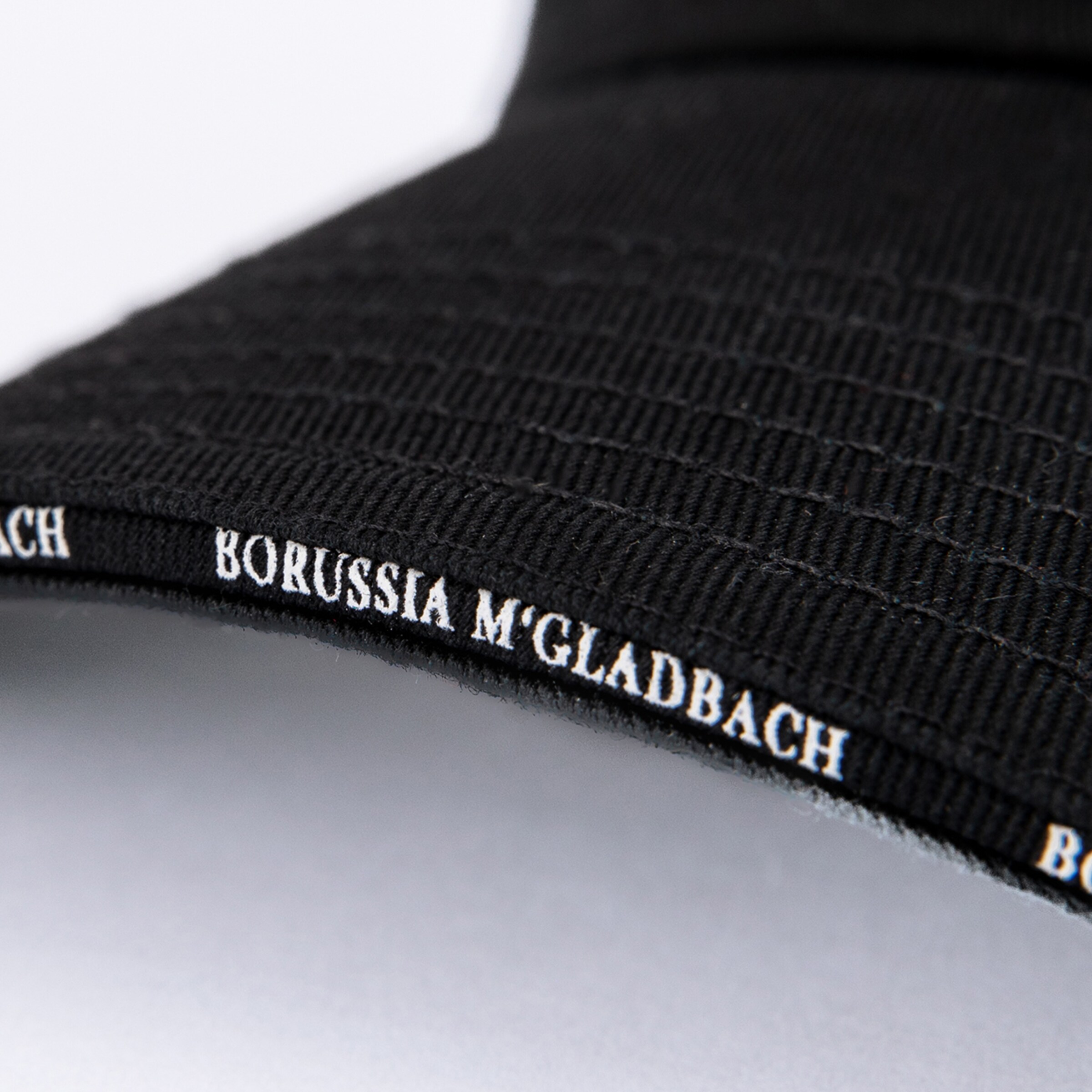 Nahaufnahme des Schirmrandes einer schwarzen Kappe mit der weißen Aufschrift „BORUSSIA M'GLADBACH“.
