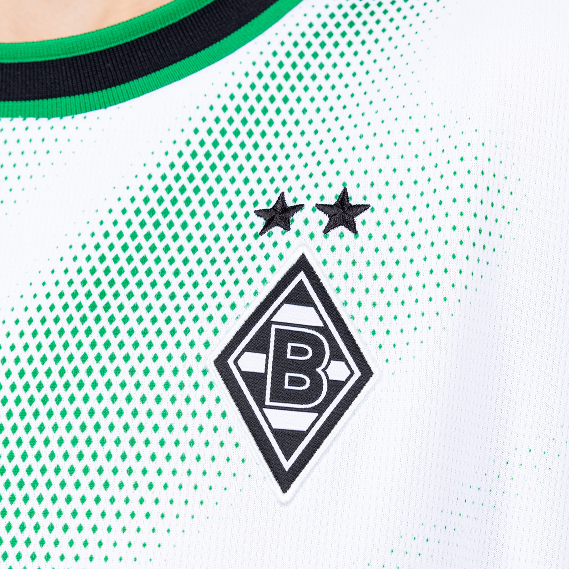 Nahaufnahme eines weißen Borussia-Mönchengladbach-Trikots mit grünem Rautenmuster, dem Vereinslogo und zwei schwarzen Sternen.