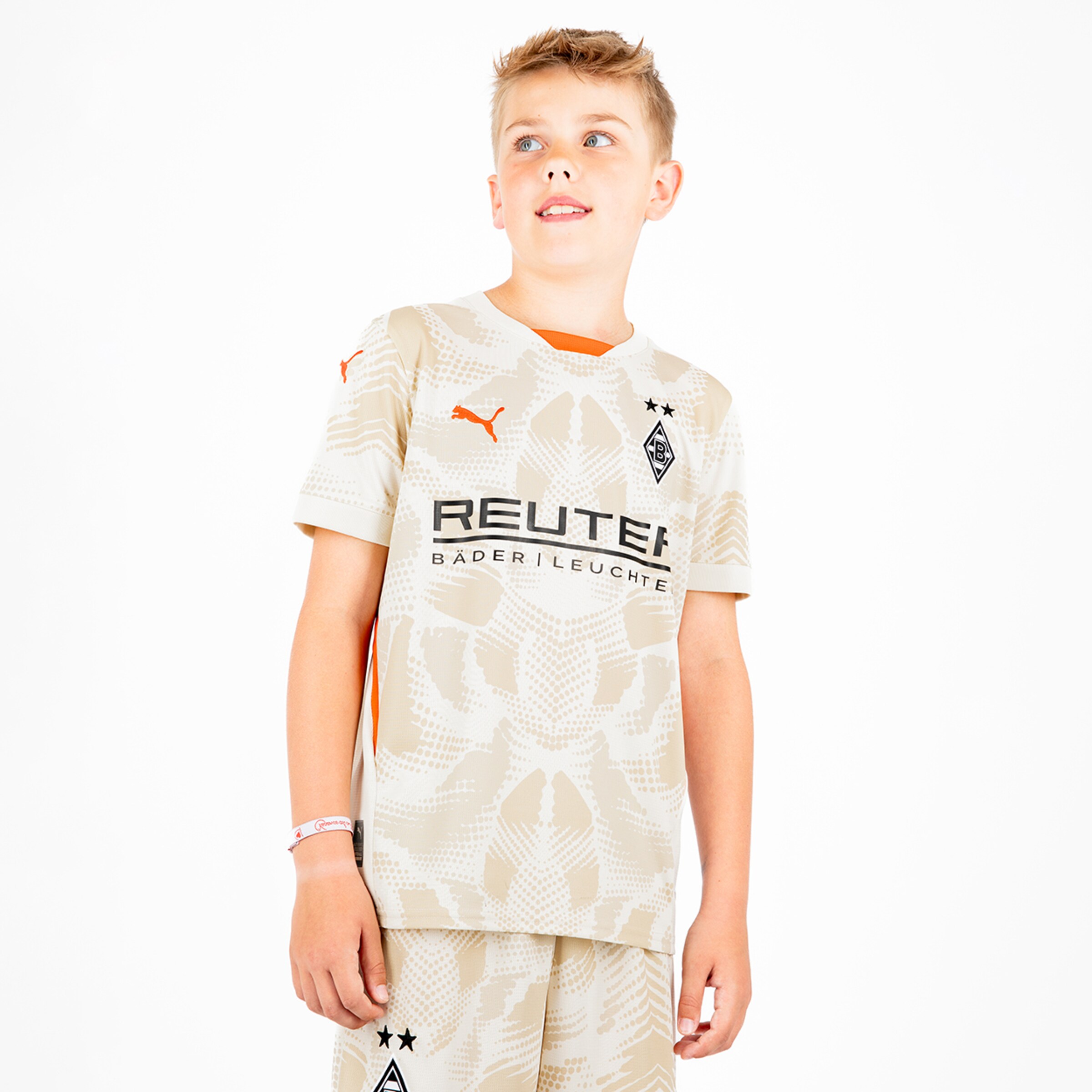 Ein Junge trägt das aktuelle Borussia Mönchengladbach Trikot in hellen Farben mit den Logos von Puma und Reuter.