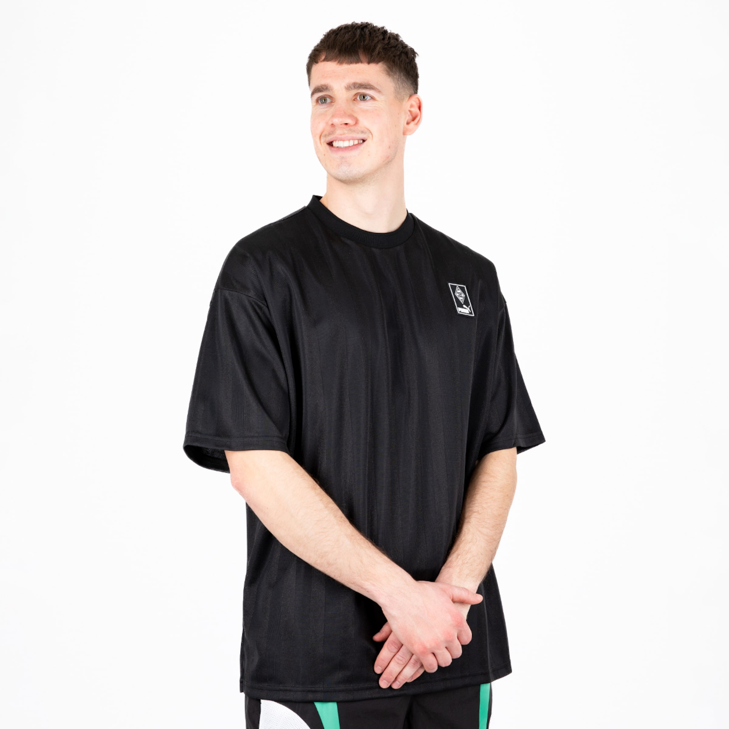 Ein junger Mann trägt ein schwarzes T-Shirt mit einem Logo und hat eine lächelnde Ausdrück.