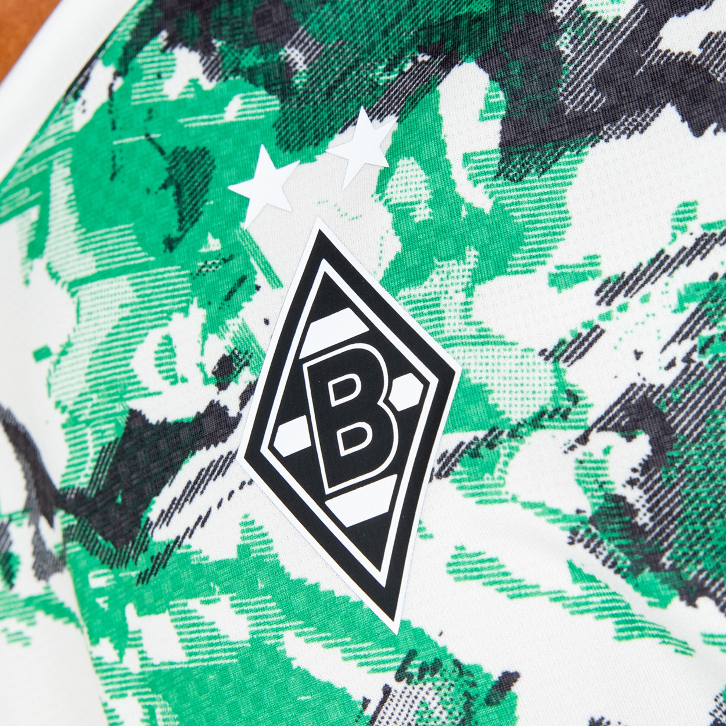 Logo von Borussia Mönchengladbach auf einem Trikot mit geometrischen Mustern in Grün und Schwarz.