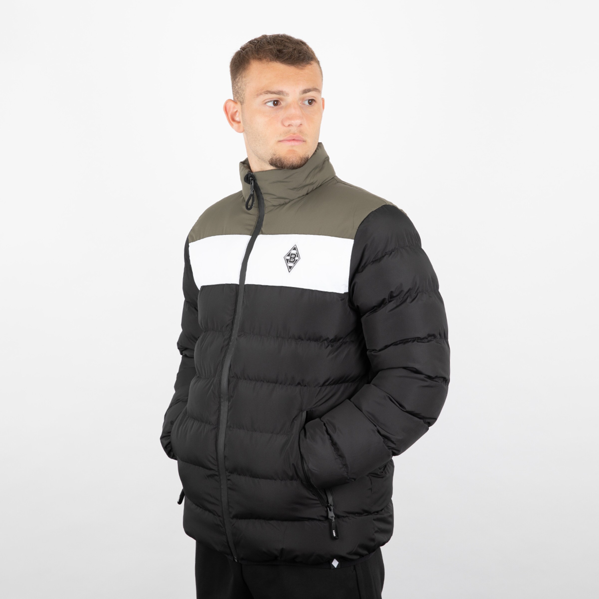 Junger Mann trägt eine schwarze und graue gesteppte Jacke mit Logo auf der Brust.