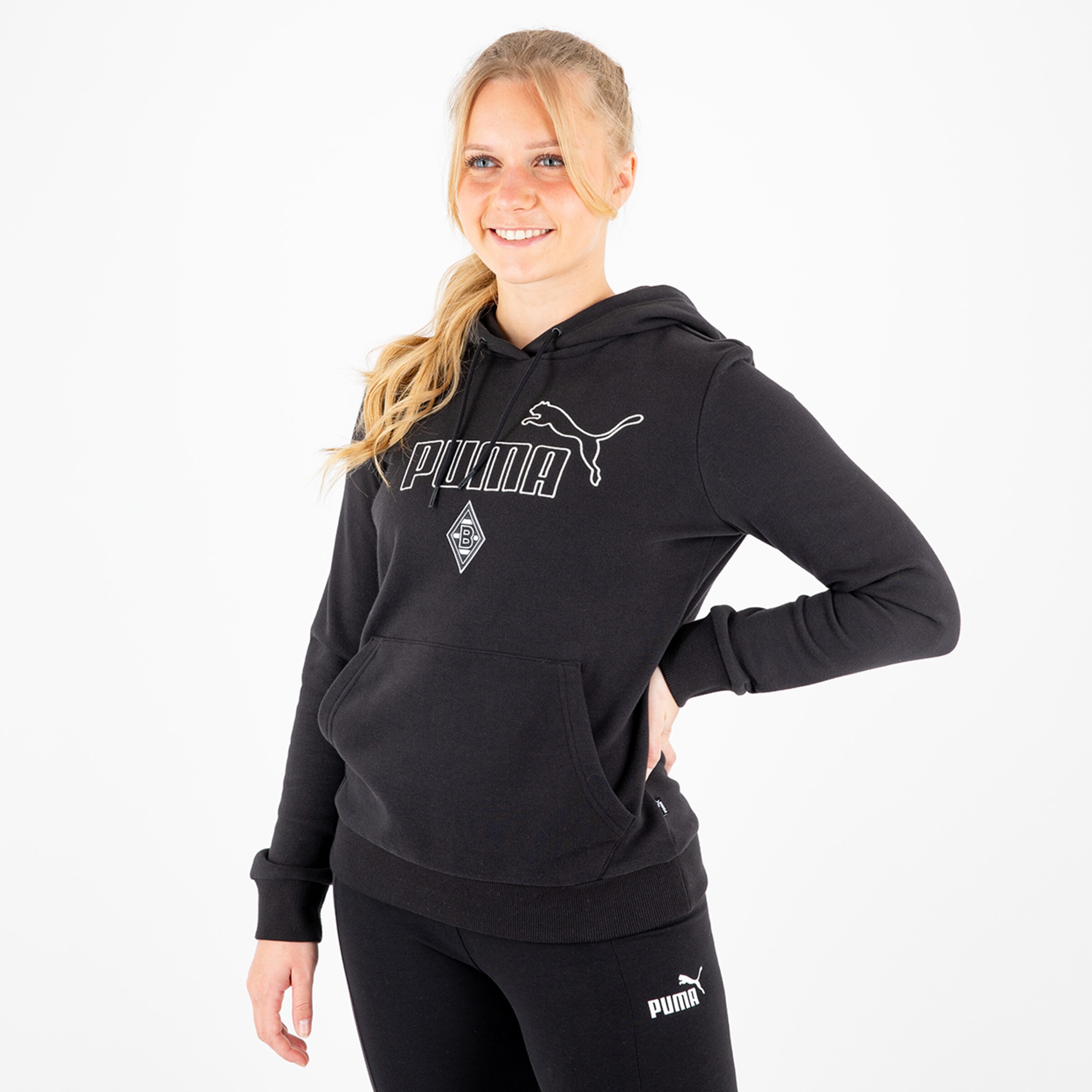 Eine junge Frau trägt einen schwarzen Kapuzenpullover mit dem PUMA-Logo und dem Borussia Mönchengladbach-Wappen.