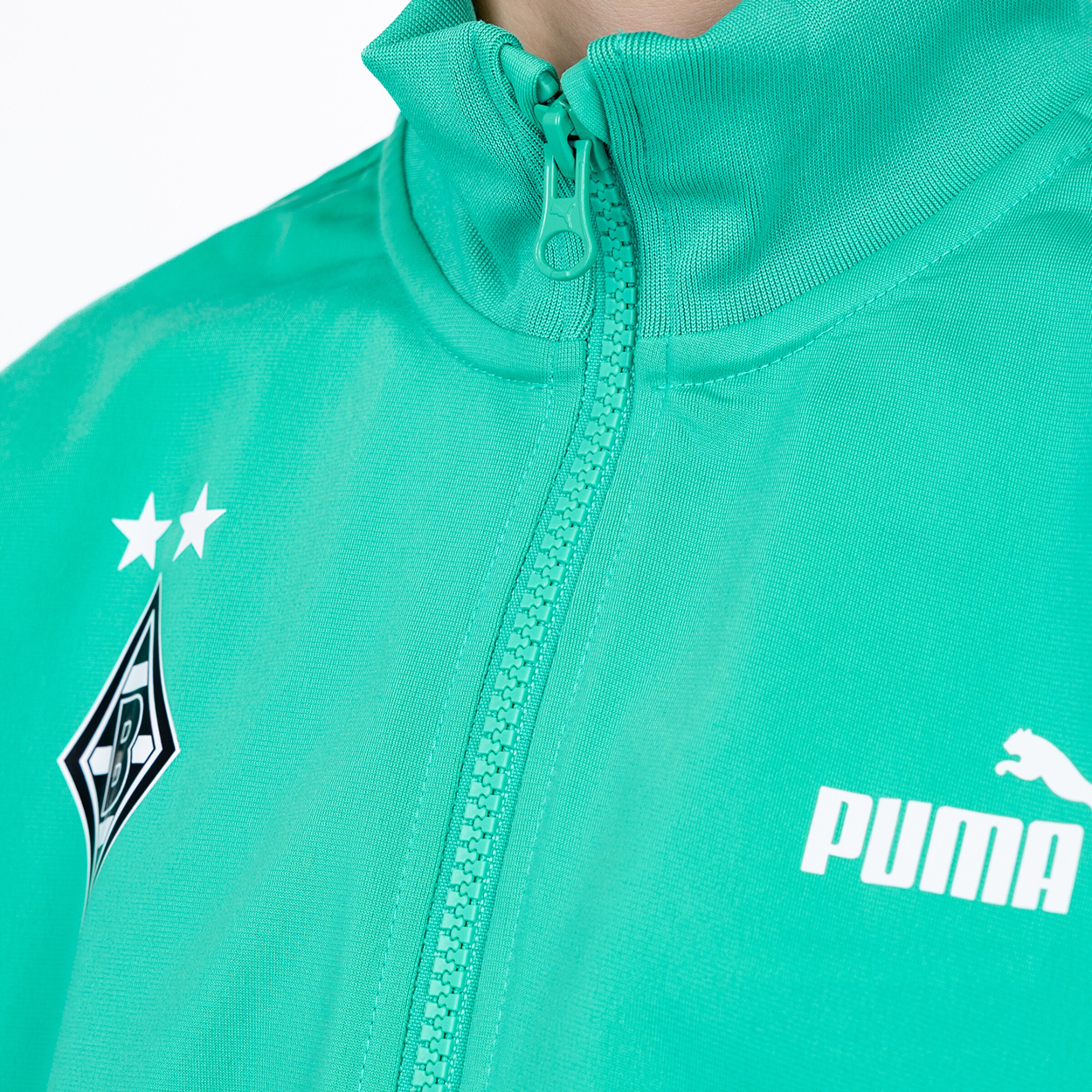 Close-up of a teal Puma track jacket with the Borussia Mönchengladbach crest, two stars, and white Puma logo.