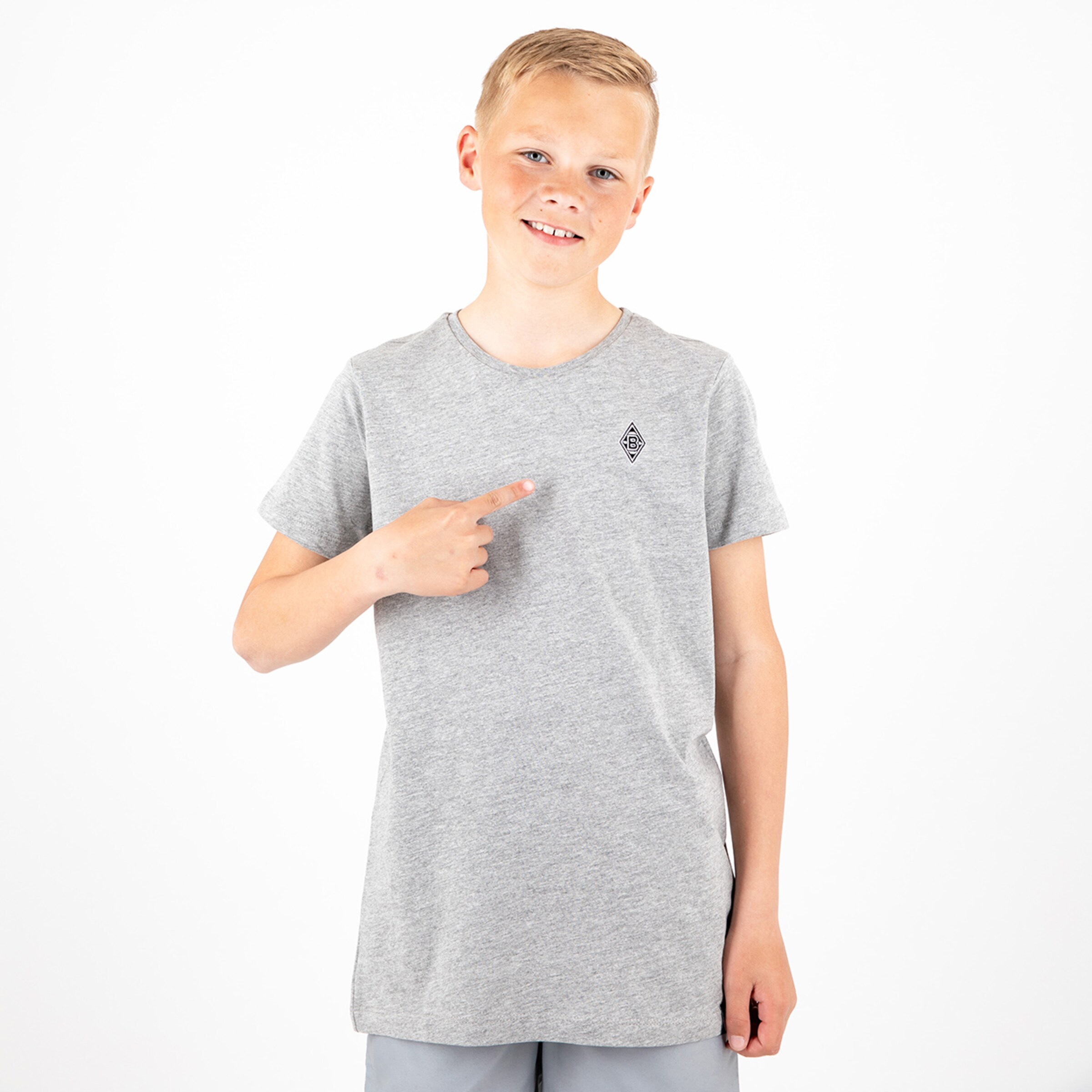 Ein Junge zeigt auf das Logo von Borussia Mönchengladbach auf seinem grauen T-Shirt.