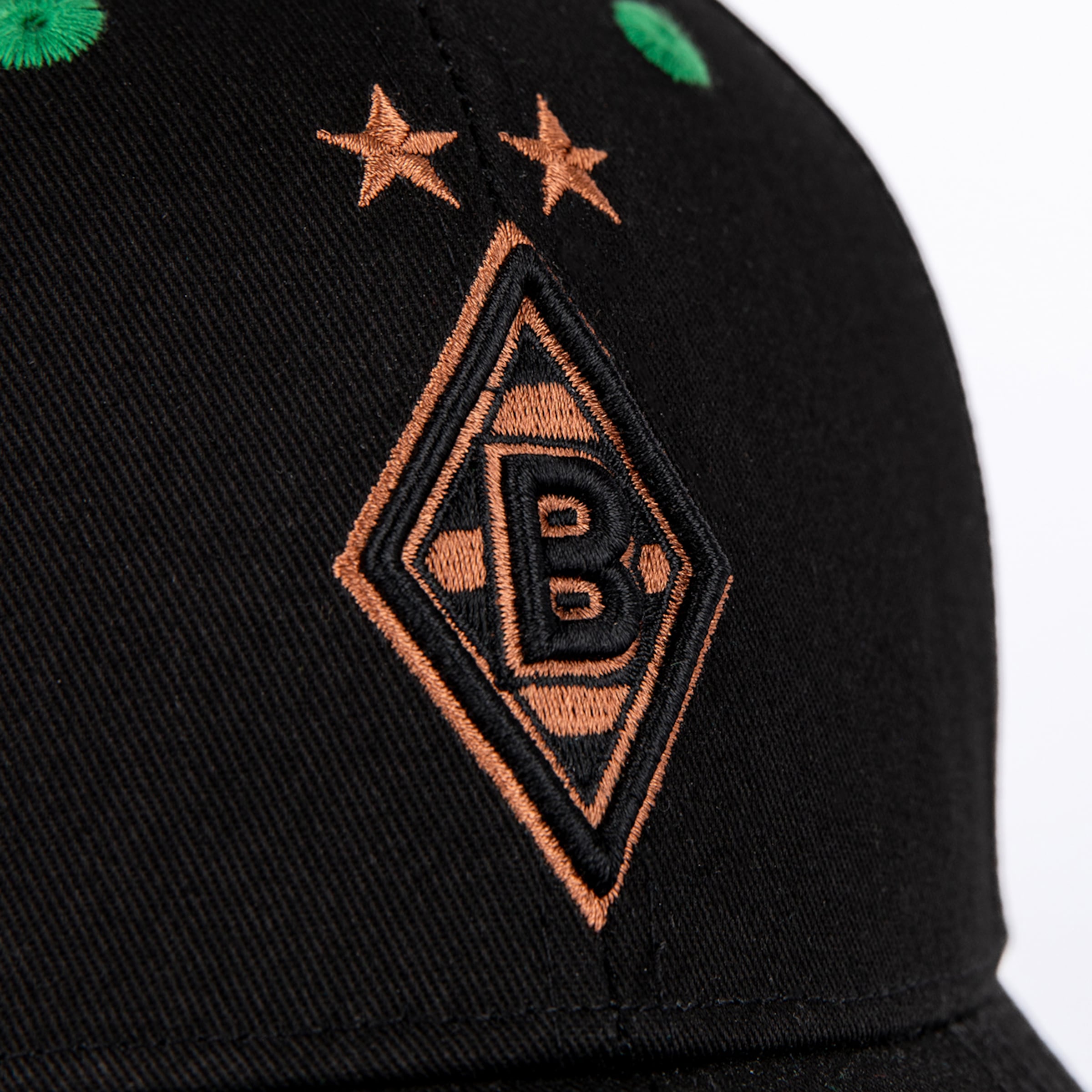 Nahaufnahme einer schwarzen Cap mit kupferfarbenem Borussia Mönchengladbach Logo (Raute mit B) und zwei Sternen darüber.