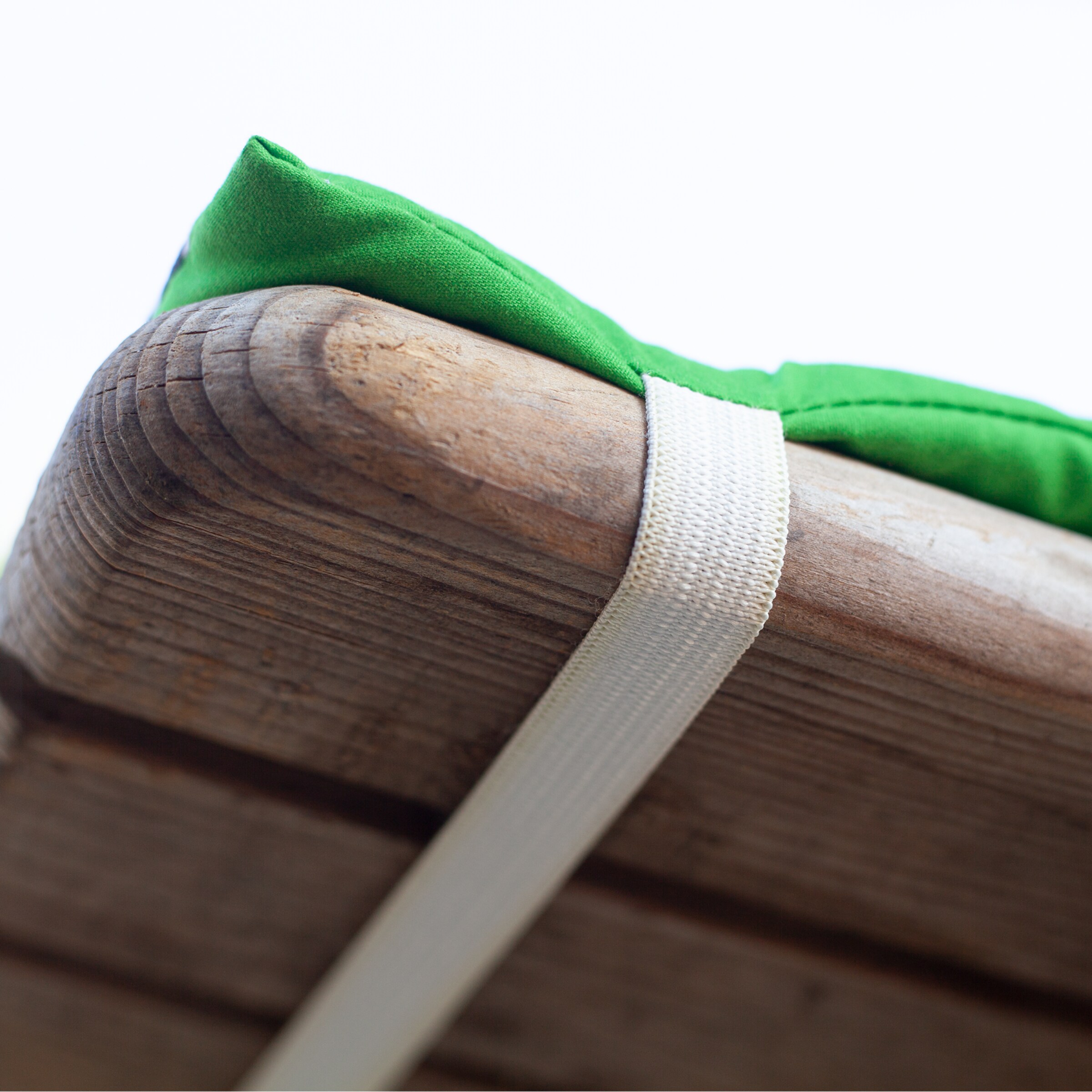 Close-up of a green cushion secured to a wooden slat with a white elastic strap.