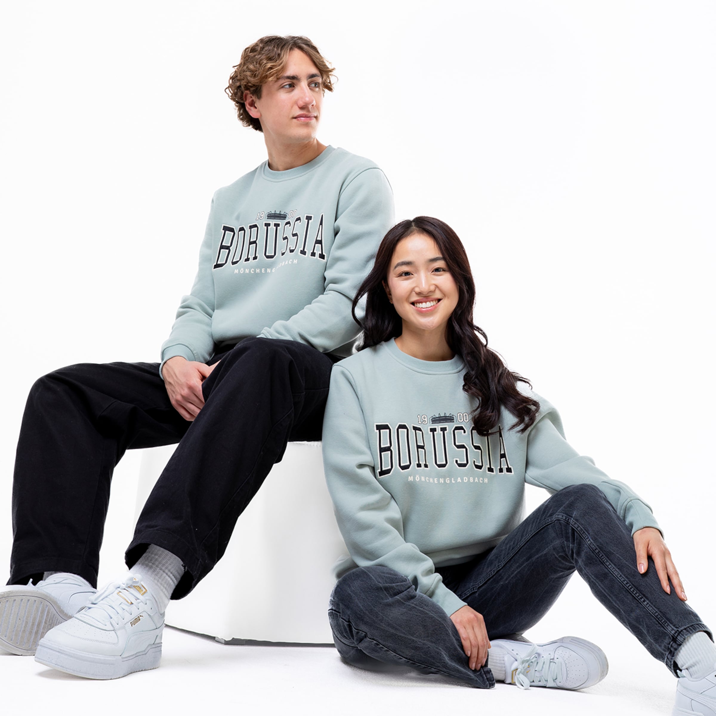 Ein Mann und eine Frau sitzen nebeneinander beide tragen graue Sweatshirts mit dem Schriftzug BORUSSIA.