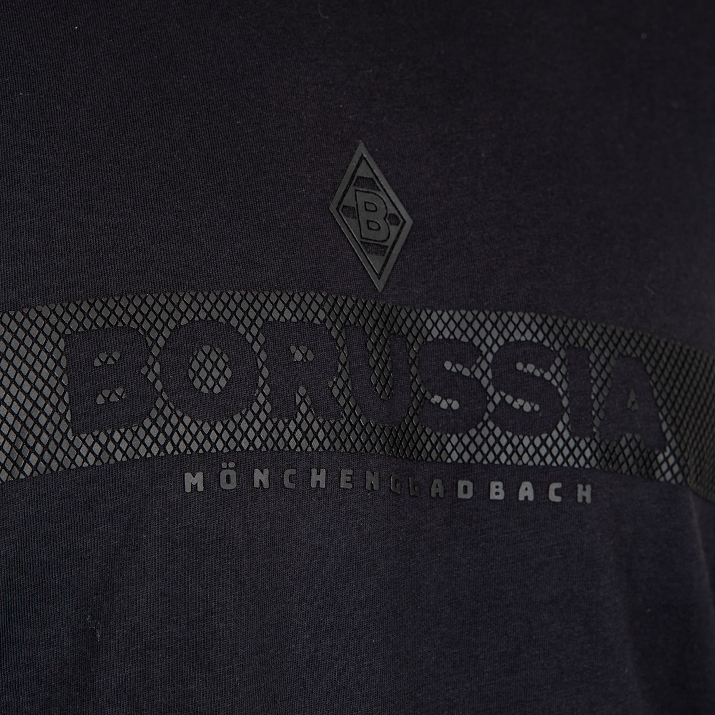 Nahaufnahme eines schwarzen Shirts mit Borussia Mönchengladbach Logo und Schriftzug in Ton-in-Ton-Optik auf einem strukturierten Band.
