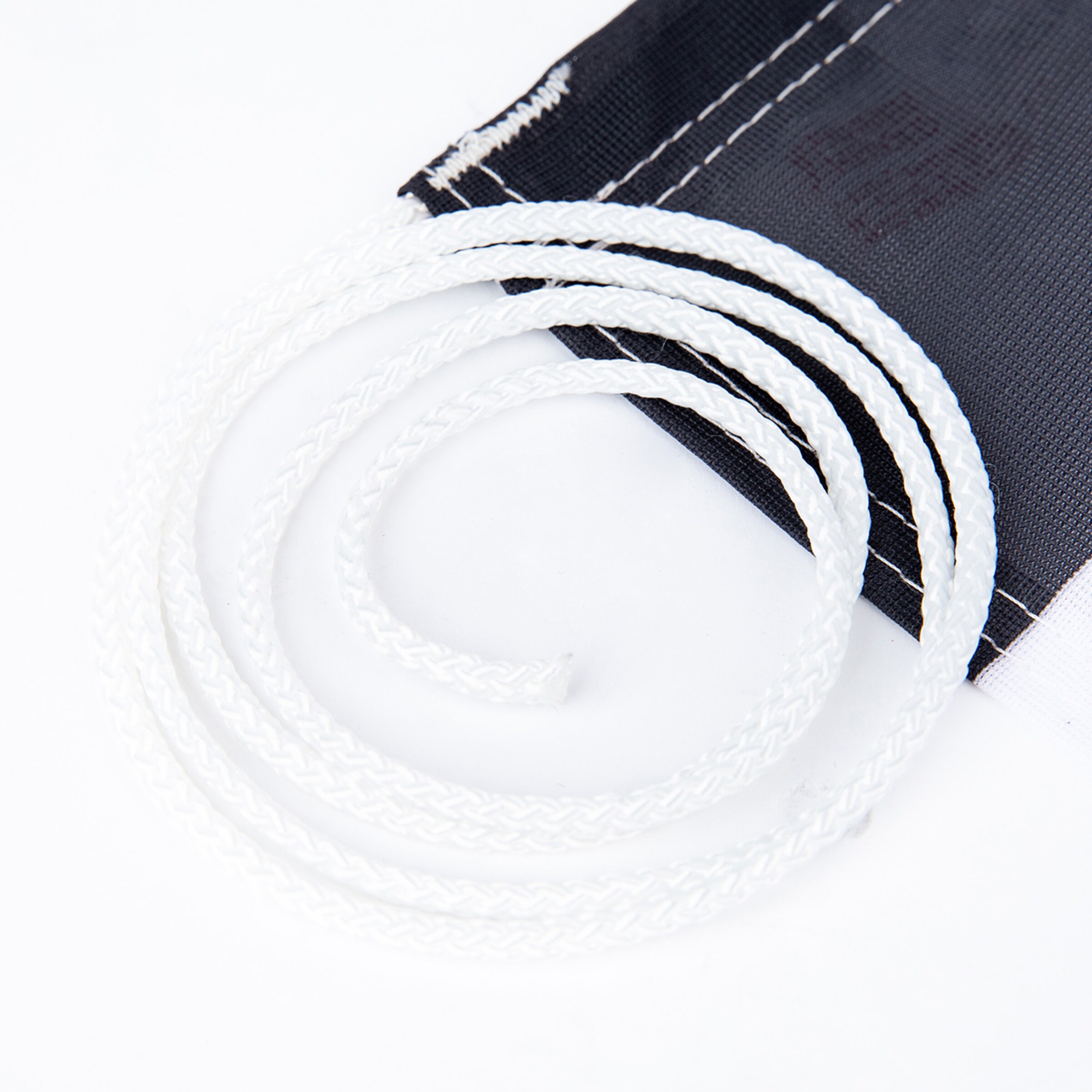 Weiße Kordel gebogen und zusammengewickelt liegt auf einem schwarzen Stoffstück.