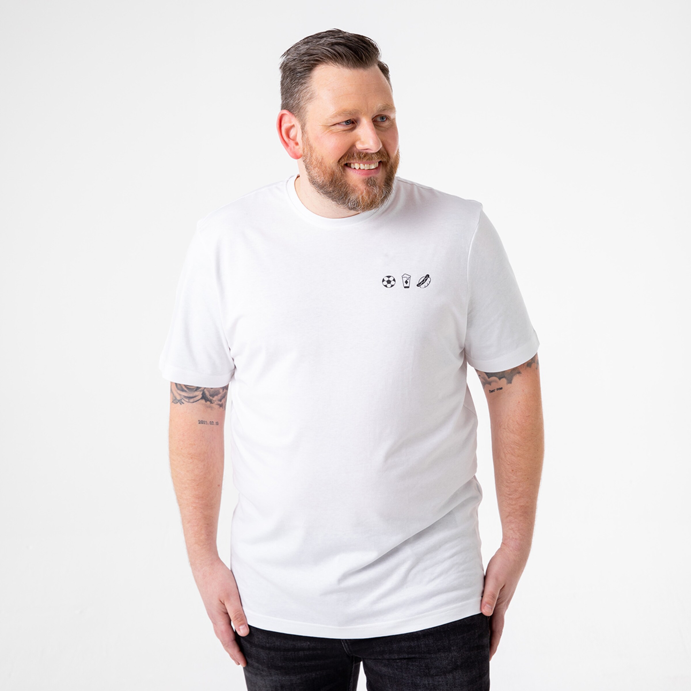 Ein Mann in einem weißen T-Shirt mit Sportmotiven lächelt.