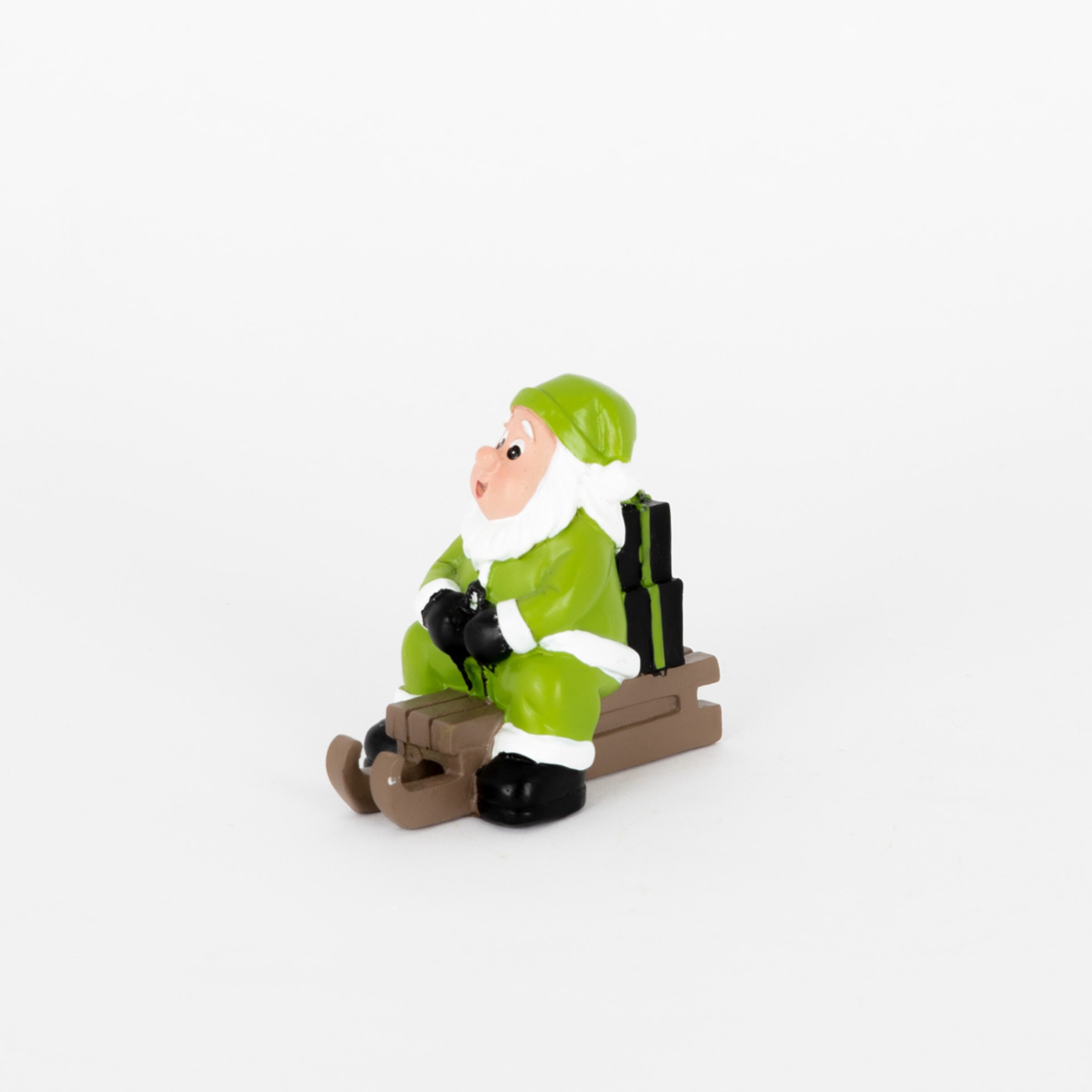 Weihnachtsmannfigur in grüner Kleidung auf einem Schlitten mit Geschenken im Hintergrund.