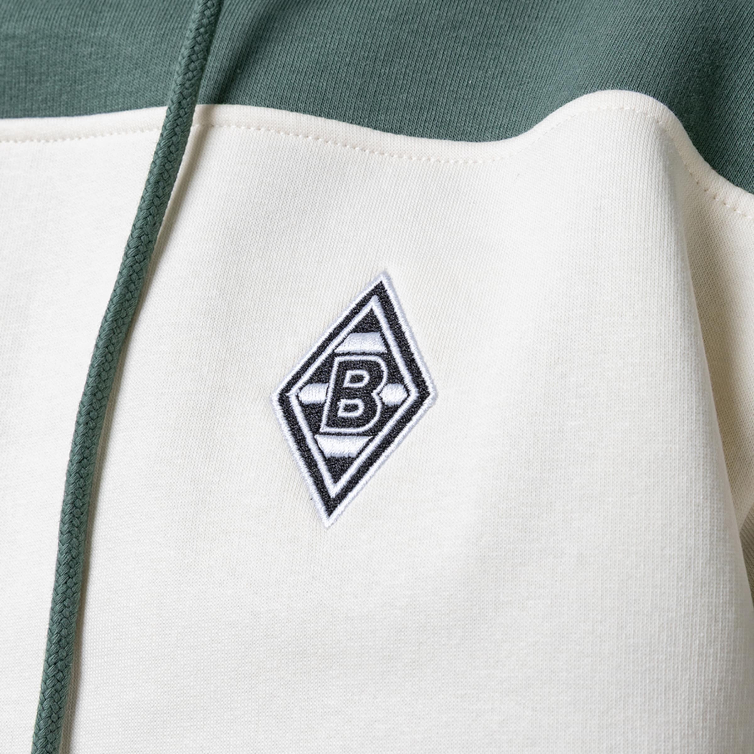 Nahaufnahme eines grün-weißen Hoodies mit dem aufgestickten Logo von Borussia Mönchengladbach.