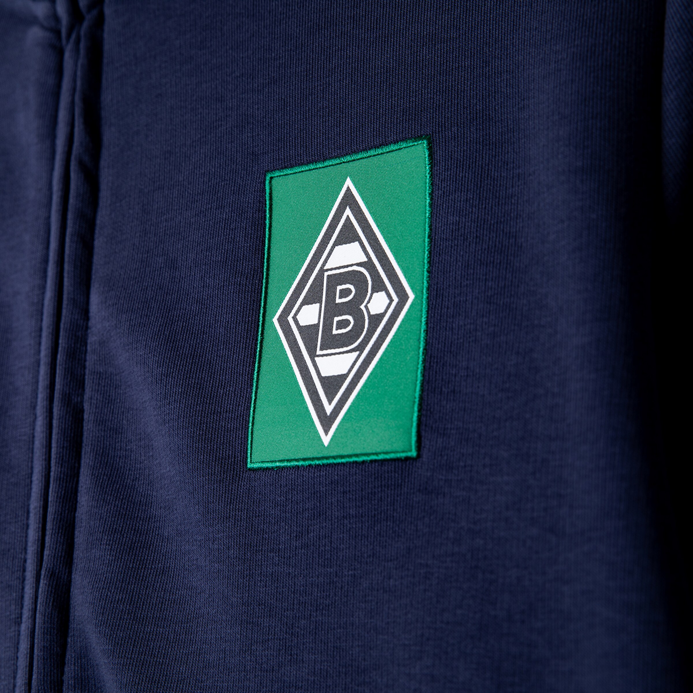 Nahaufnahme einer dunkelblauen Jacke mit dem Rauten-Logo von Borussia Mönchengladbach auf einem grünen Aufnäher.