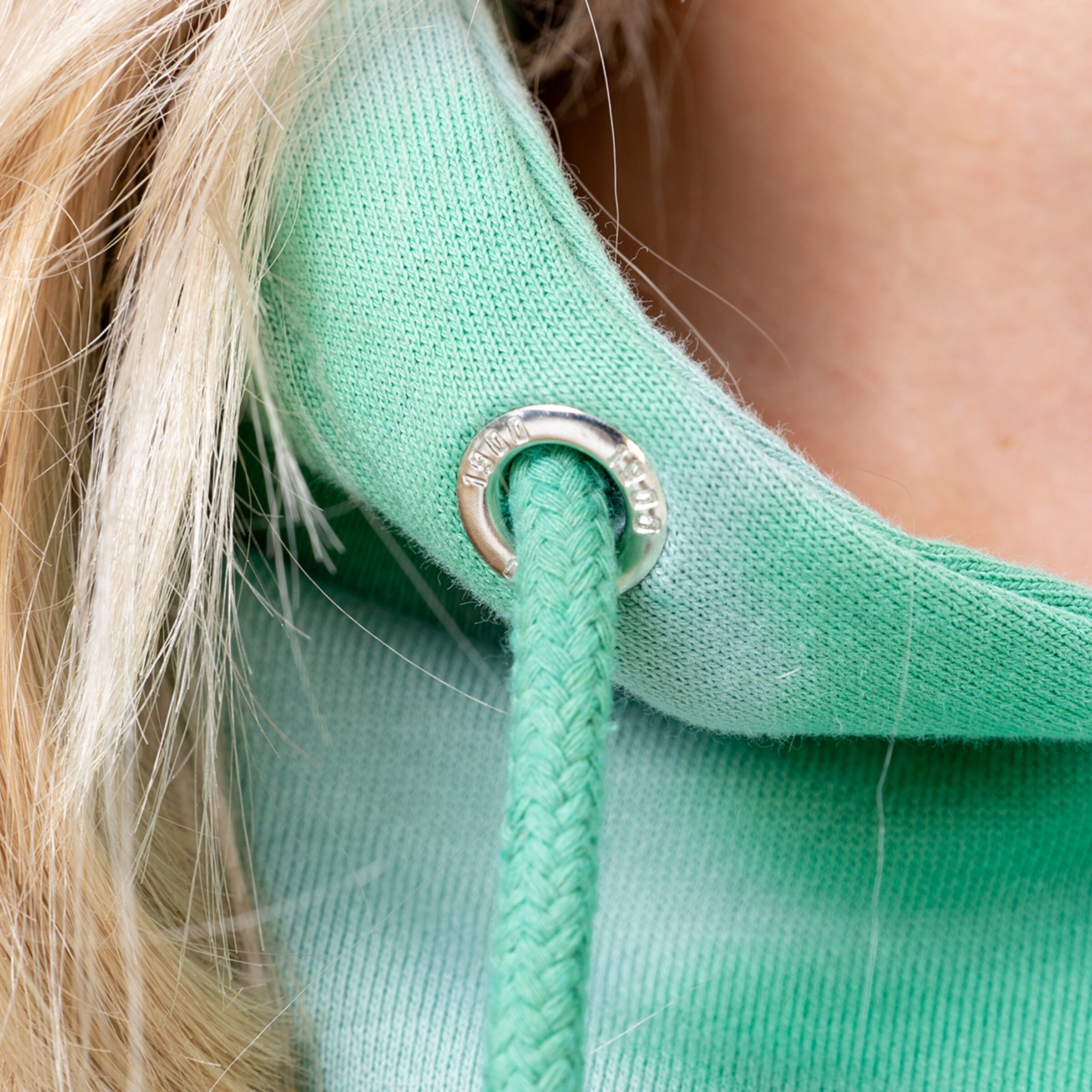 Close-up of a green hoodie featuring a cord and two-part eyelet fastening.