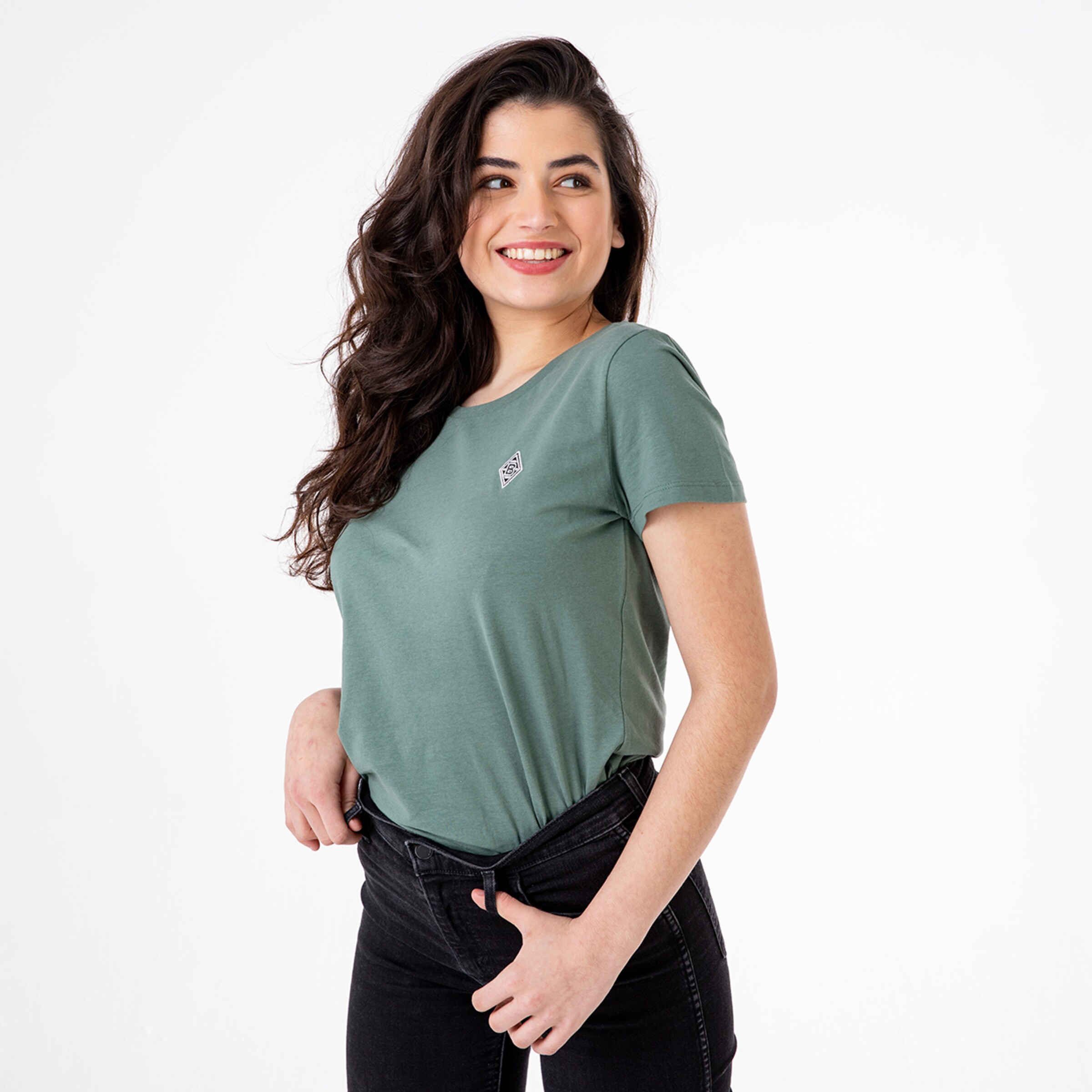 Woman wearing a green t-shirt and black jeans smiling with one hand on her hip.
