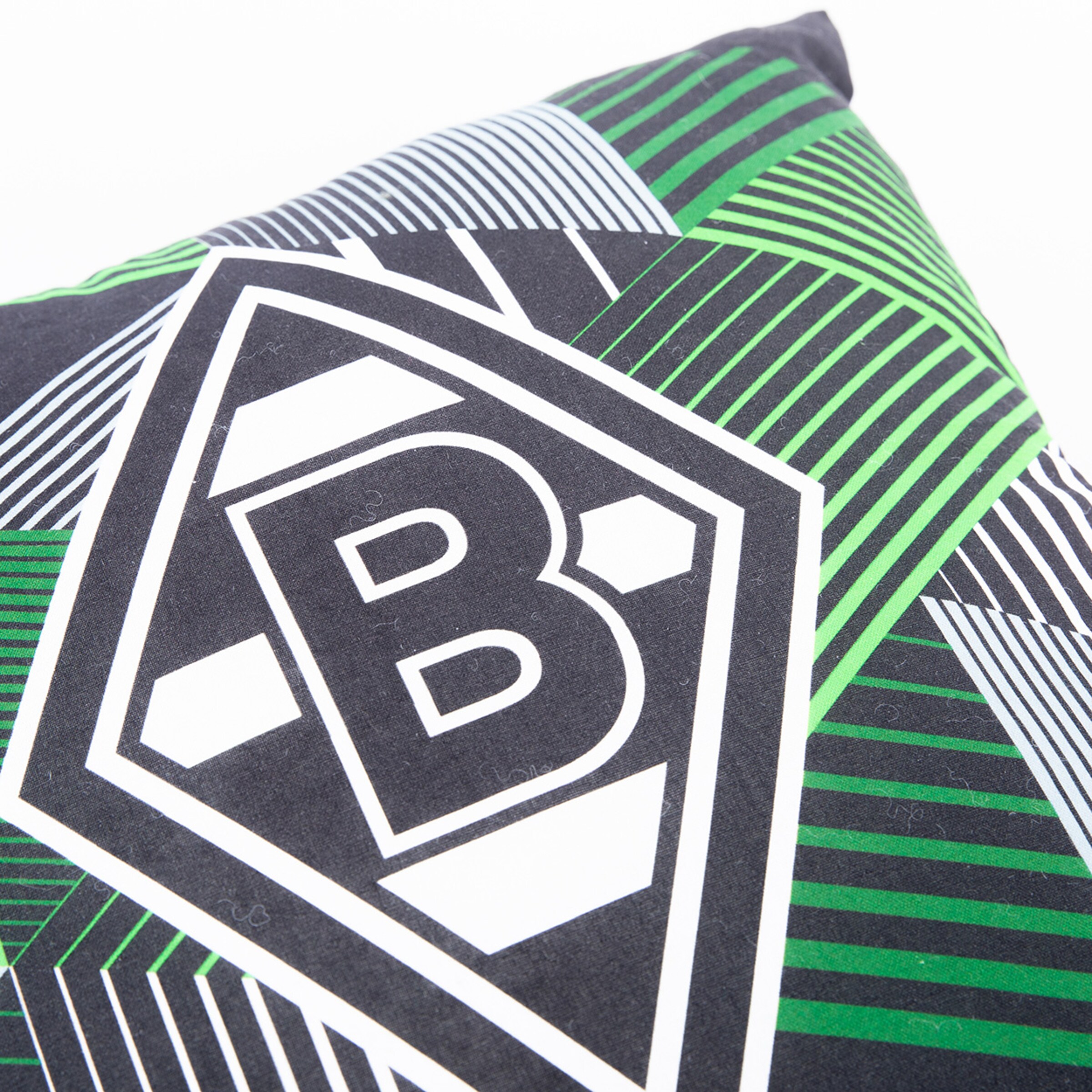 Nahaufnahme eines Kissens mit dem Borussia Mönchengladbach Logo auf einem grün-schwarz-weißen geometrischen Muster.