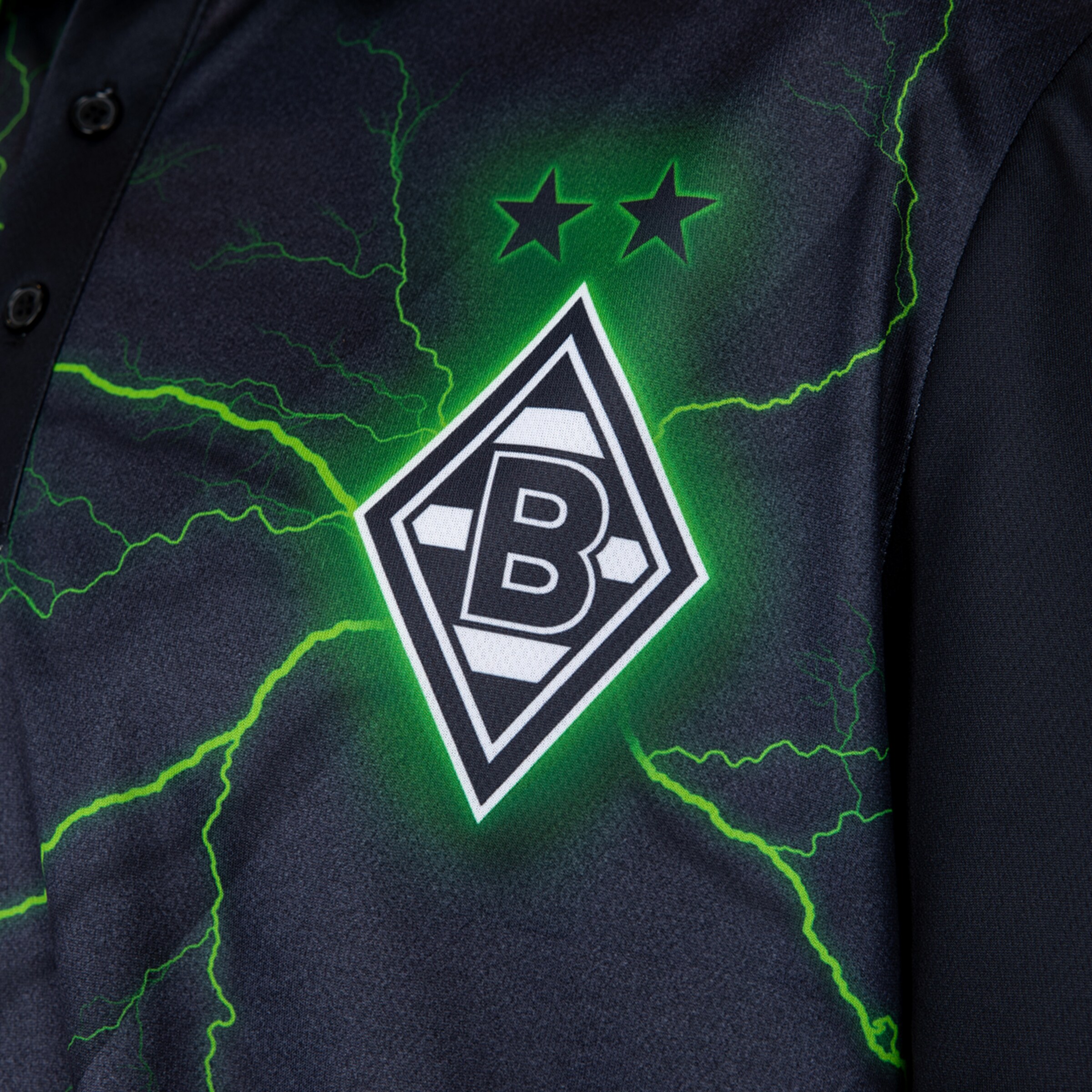 Nahaufnahme eines schwarzen Trikots mit dem Logo von Borussia Mönchengladbach, zwei Sternen und leuchtend grünen Blitzen.
