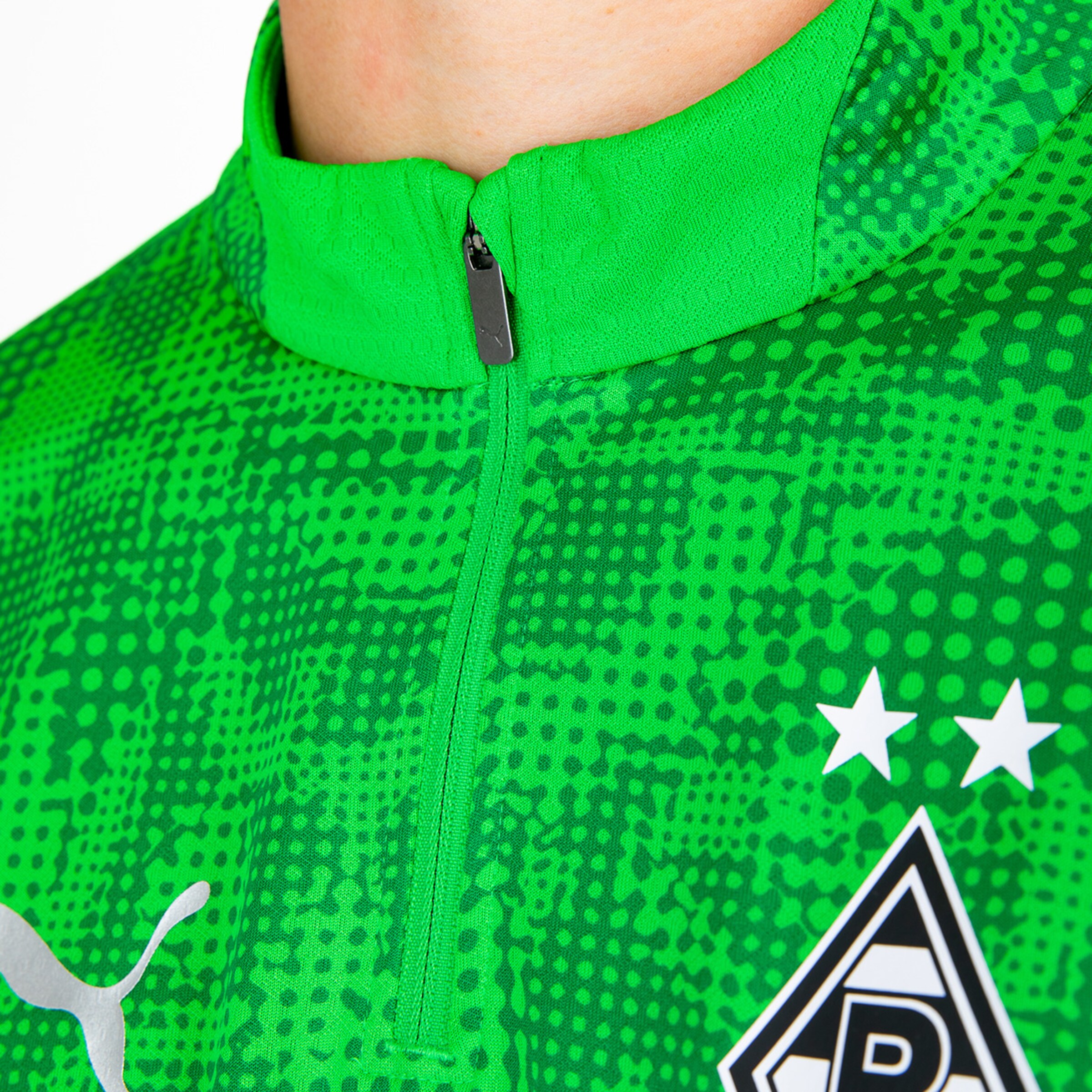 Ausschnitt einer grünen Fußballjacke mit Reißverschluss und einem Logo.