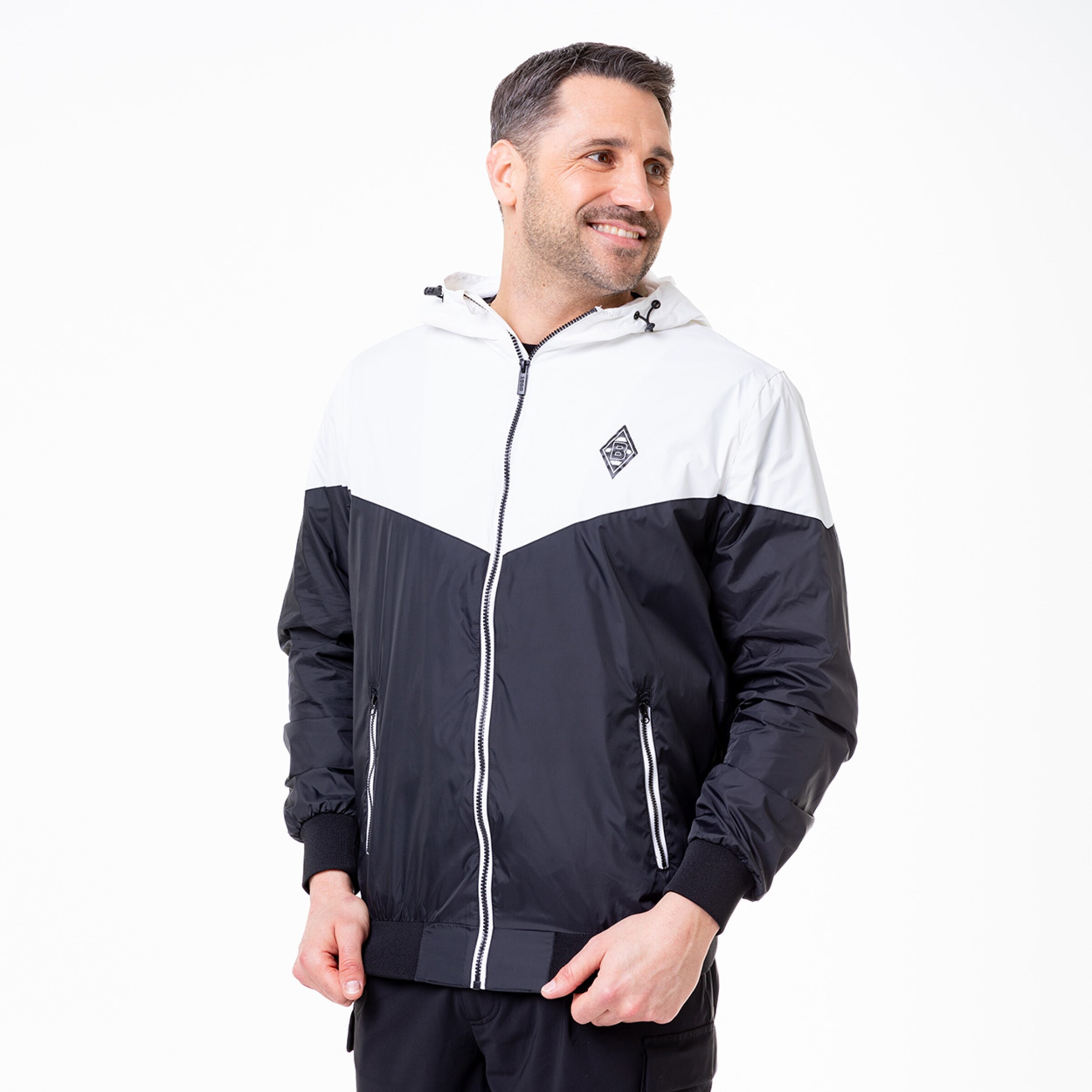 Man in a sporty hooded jacket smiling and standing slightly to the side.
