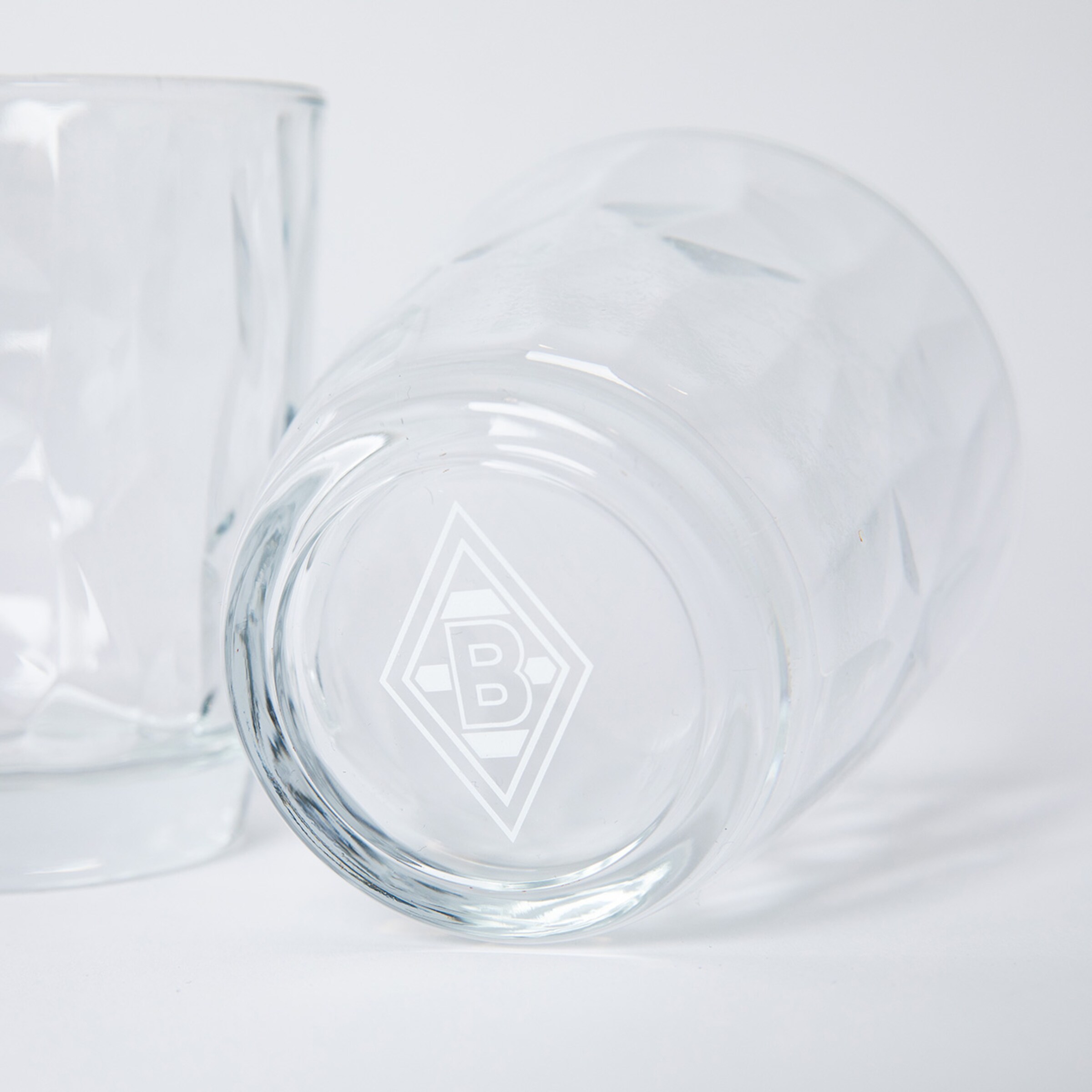 Zwei strukturierte Gläser vor weißem Hintergrund. Ein liegendes Glas zeigt auf dem Boden das Logo von Borussia Mönchengladbach.
