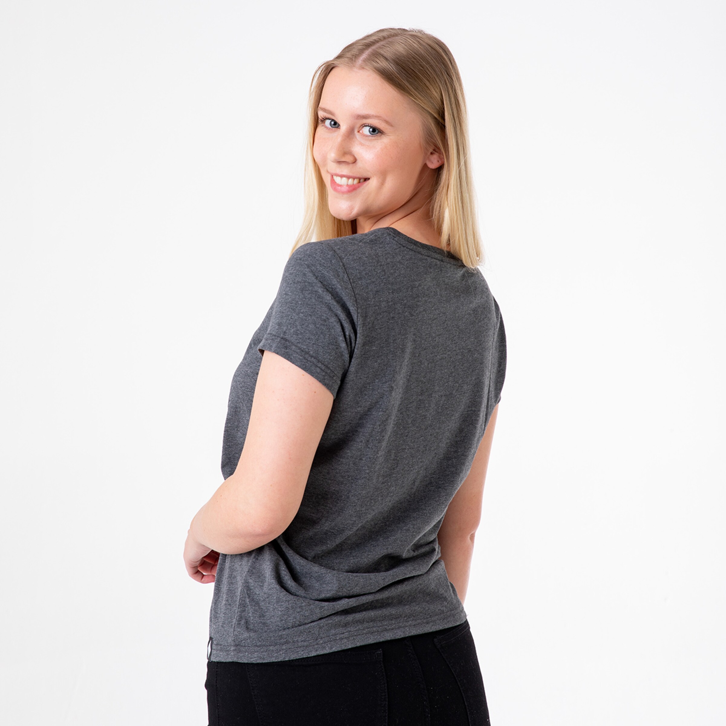 A woman with long blonde hair smiles over her shoulder wearing a gray t-shirt.
