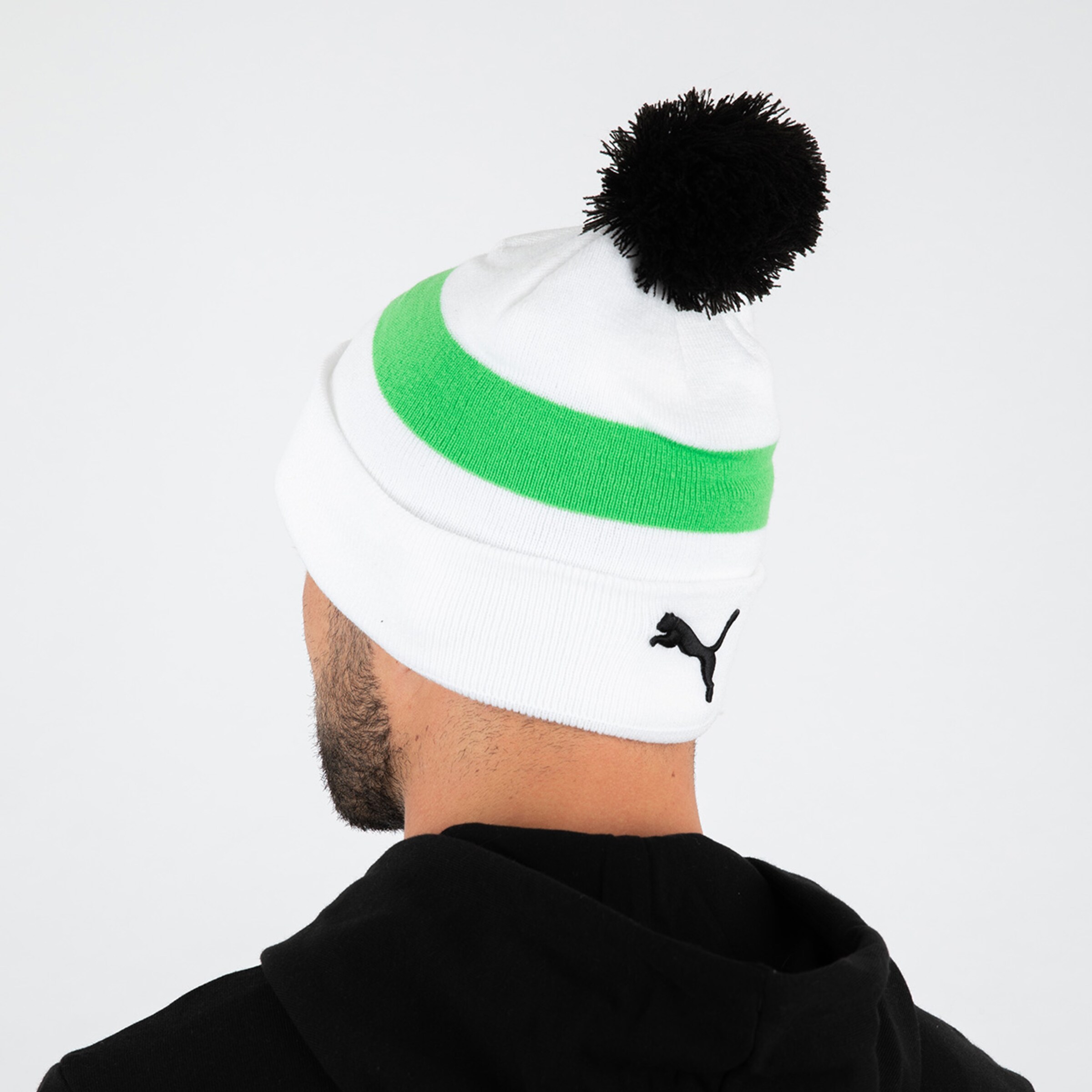 Kopfbedeckung in Weiß mit grüner und schwarzer Bommel Logo von Puma sichtbar.