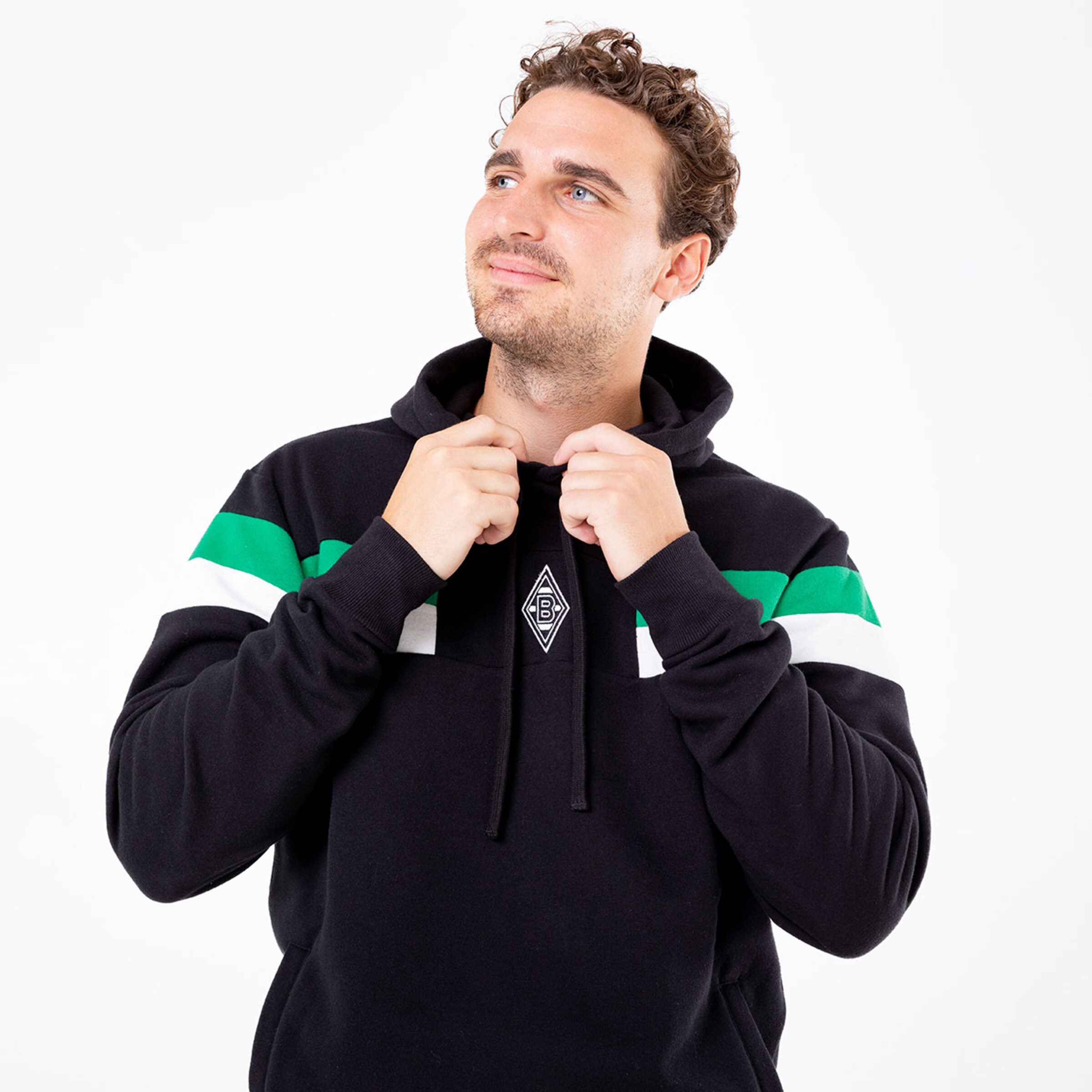 Mann in schwarzem Hoodie mit grün-weißen Streifen schaut nach oben.