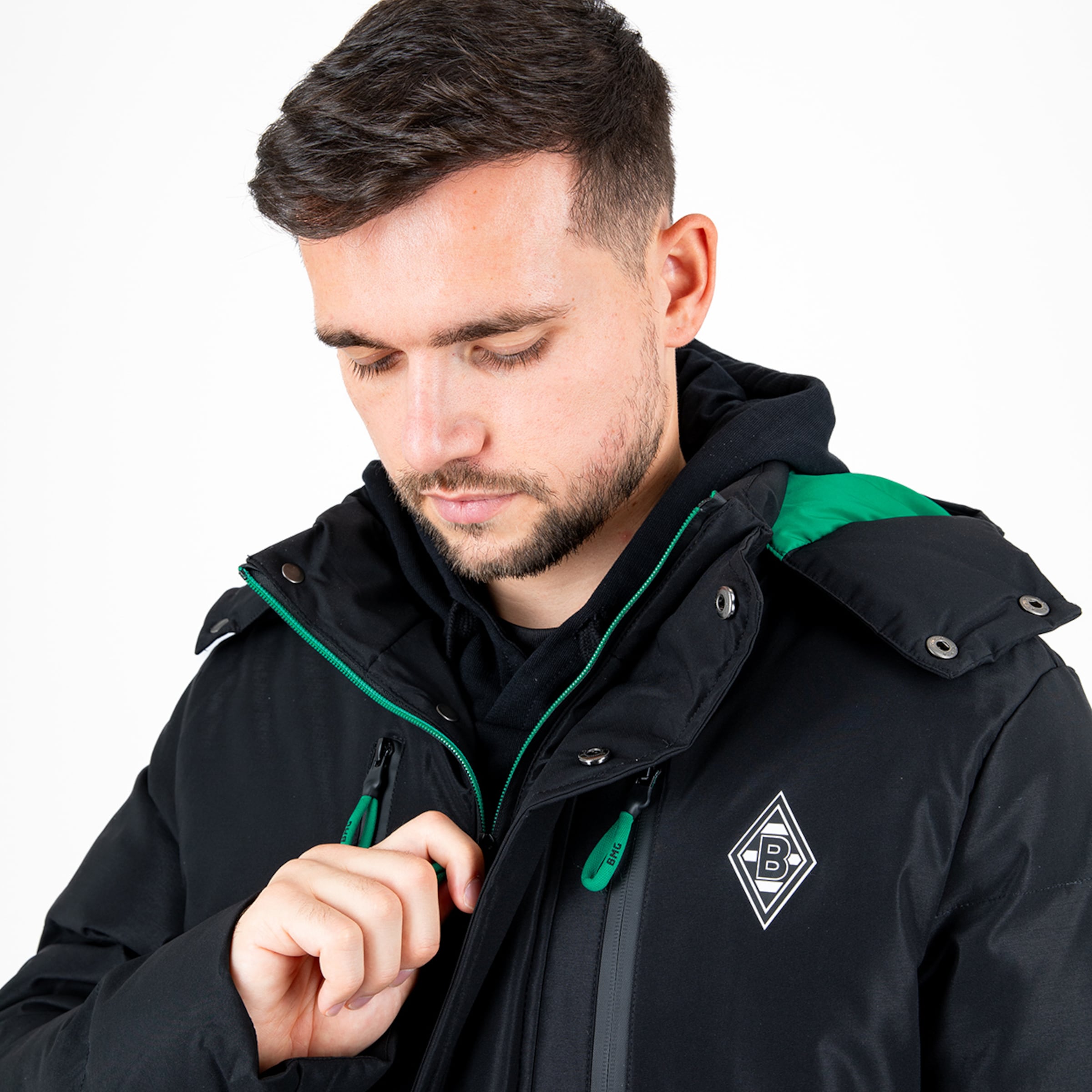 Mann in schwarzer Jacke mit grünem Kragen und Borussia Mönchengladbach Emblem zeigt eine nachdenkliche Pose.