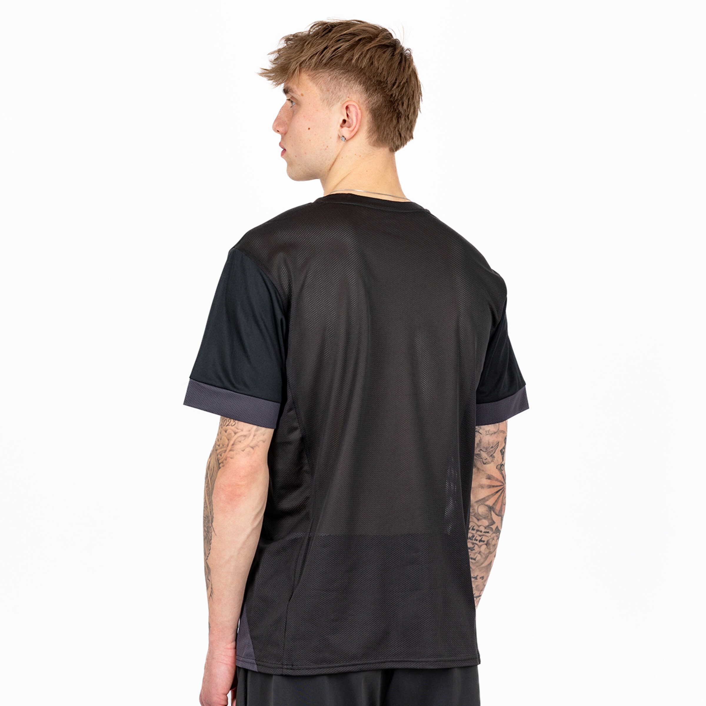 A young man with tattoos wearing a black sports jersey standing with his back to the camera.