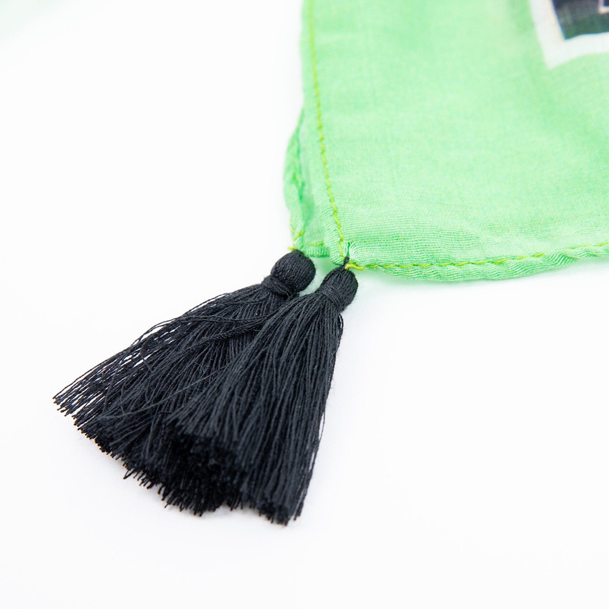 Detailaufnahme eines grünen Schals mit schwarzen Fransen.