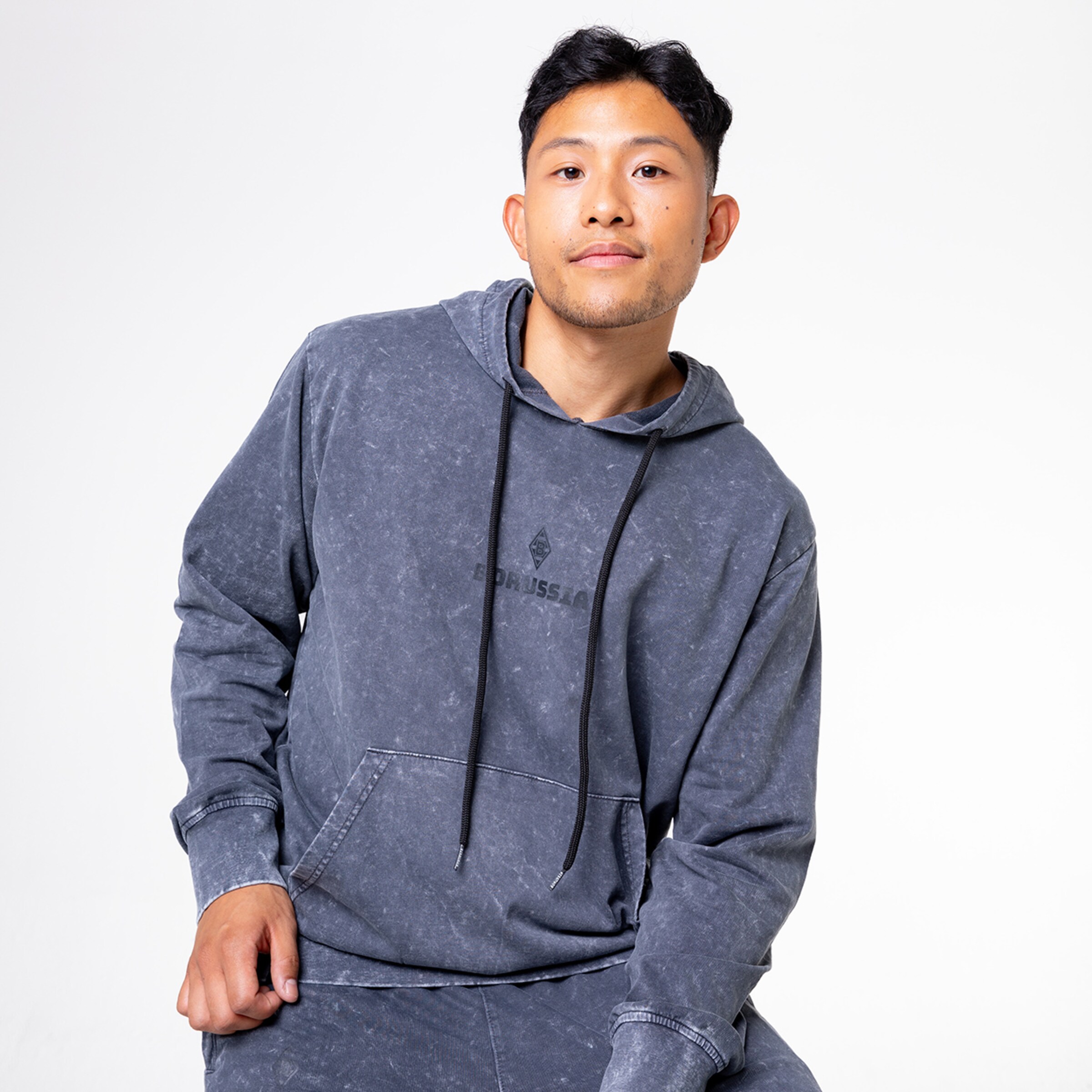 Mann in grauem Hoodie mit Kängurutasche und Schriftzug.
