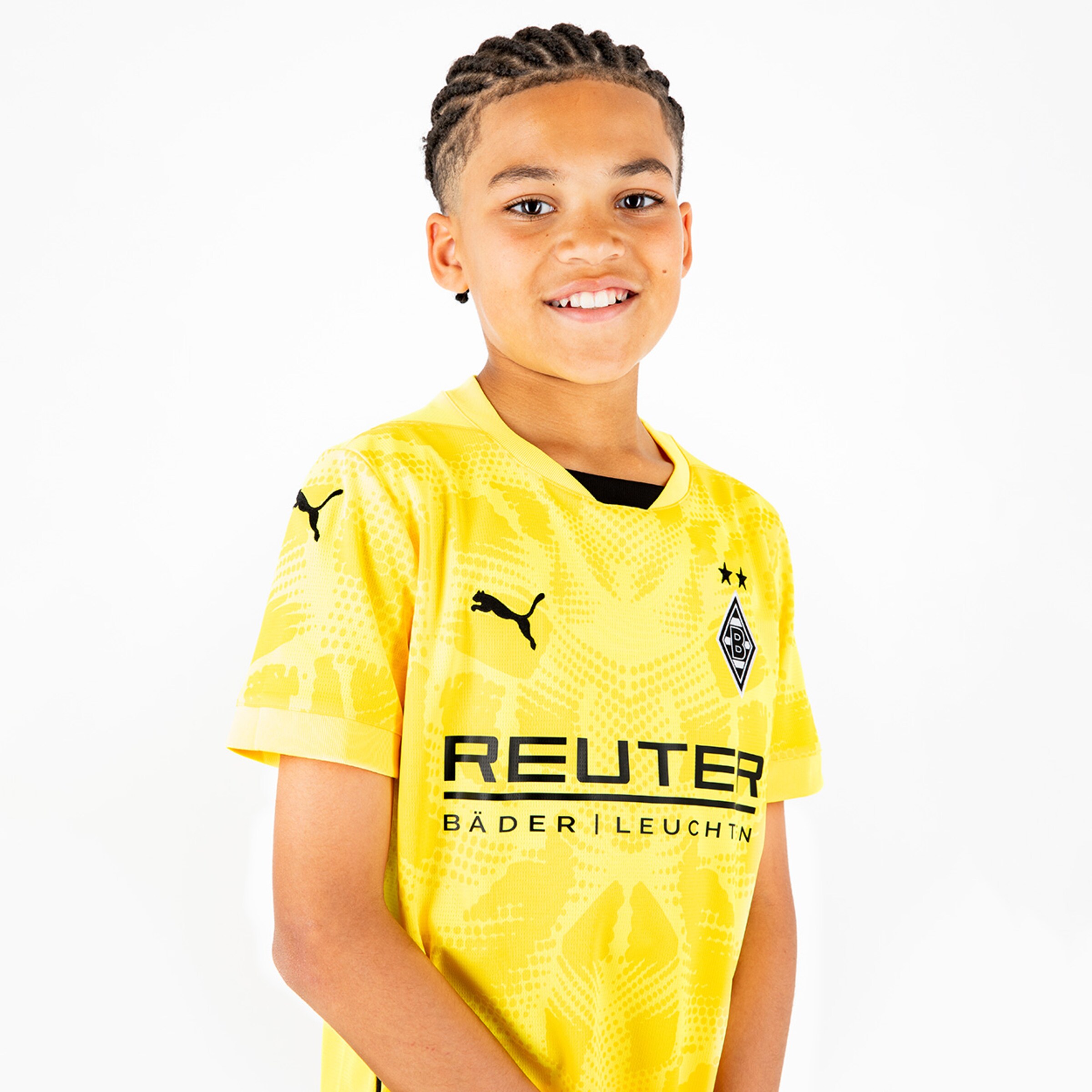 Junger Fußballer in gelbem Borussia Mönchengladbach Trikot von Puma mit geflochtenen Haaren und freundlichem Lächeln.