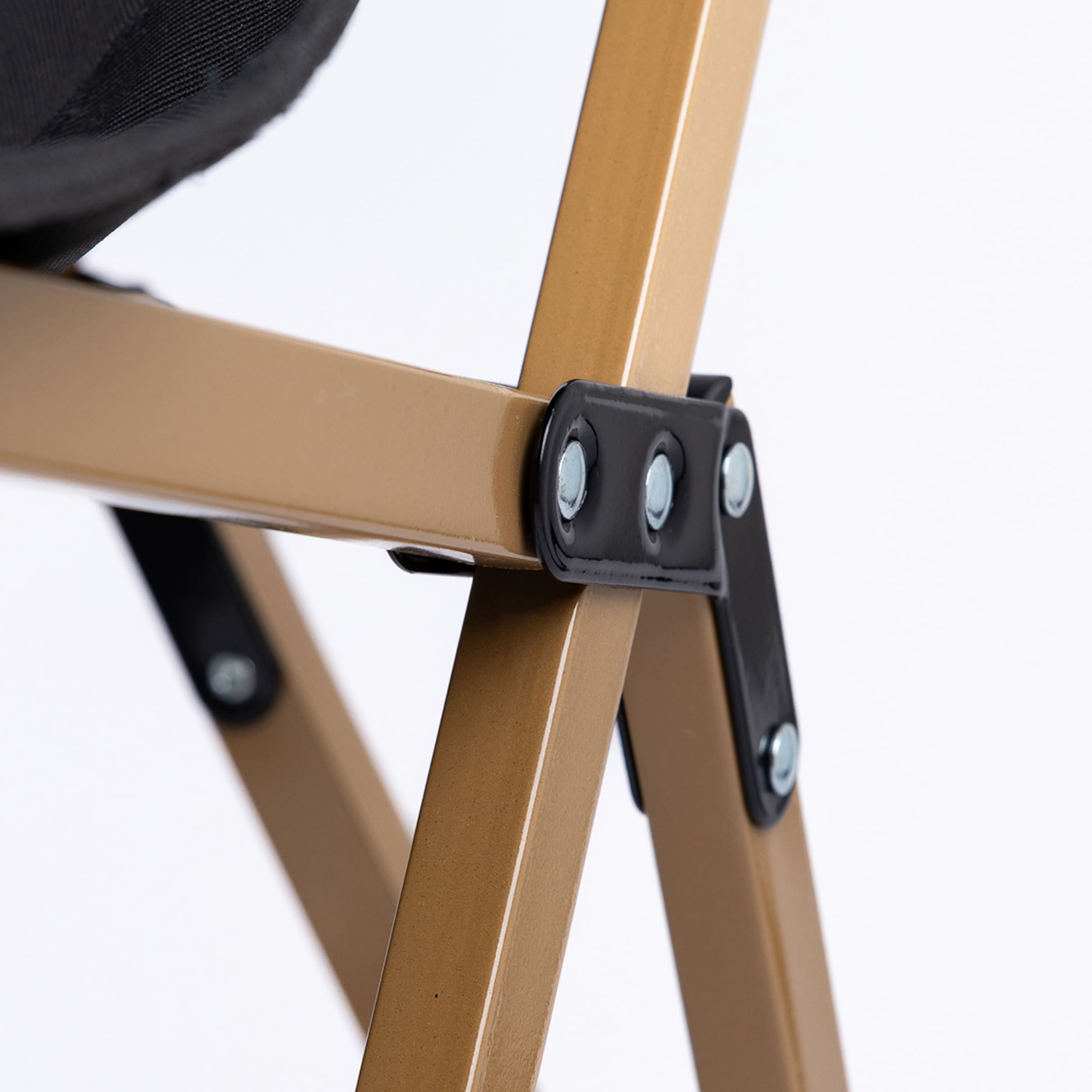 Detail eines Klappstuhl-Gelenks: Goldfarbenes Metallgestänge mit schwarzer Verbindungsklammer und silbernen Nieten vor weißem Hintergrund.