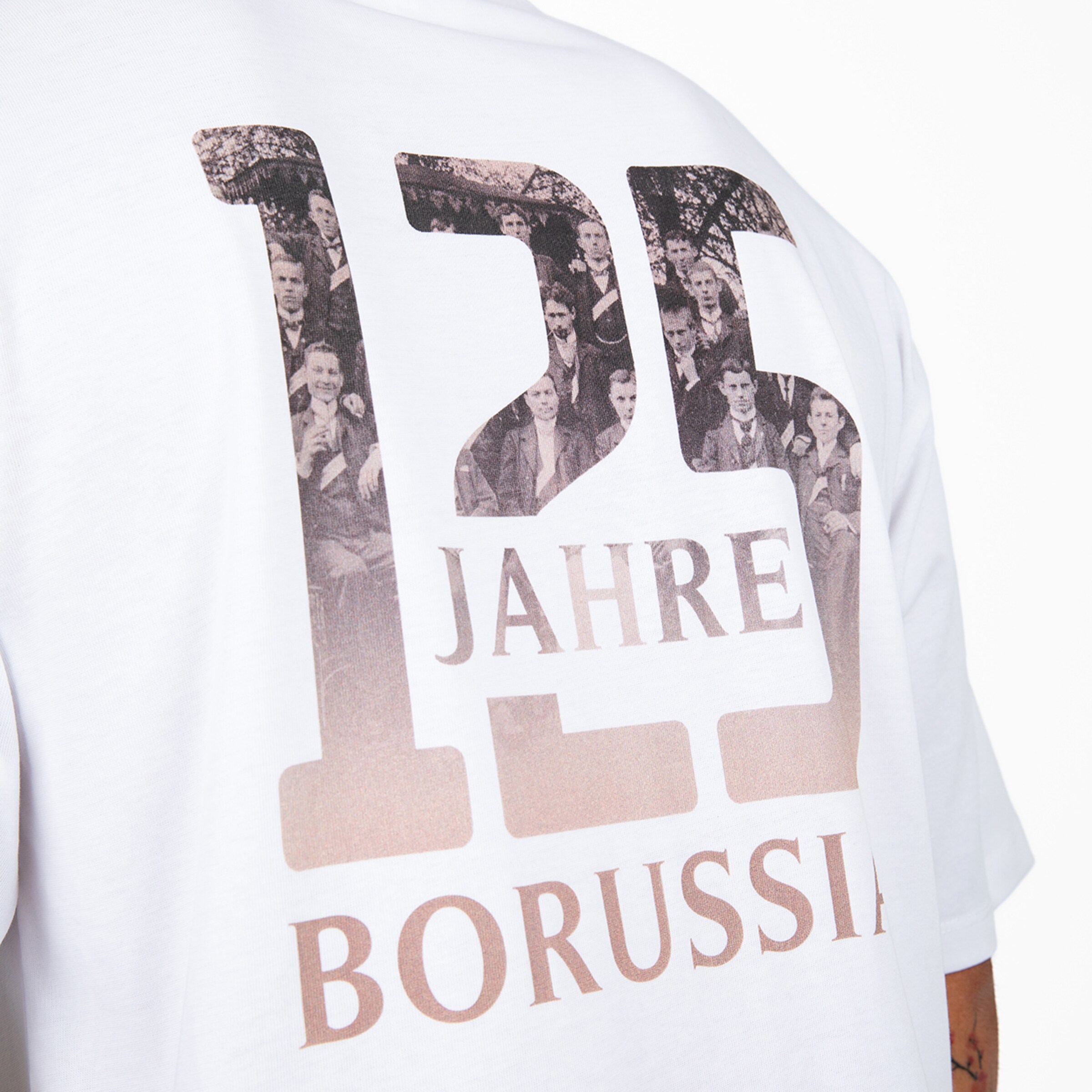 Rückansicht eines weißen T-Shirts mit „125 JAHRE BORUSSIA“-Grafik. Die Ziffern enthalten historische Schwarz-Weiß-Teamfotos.