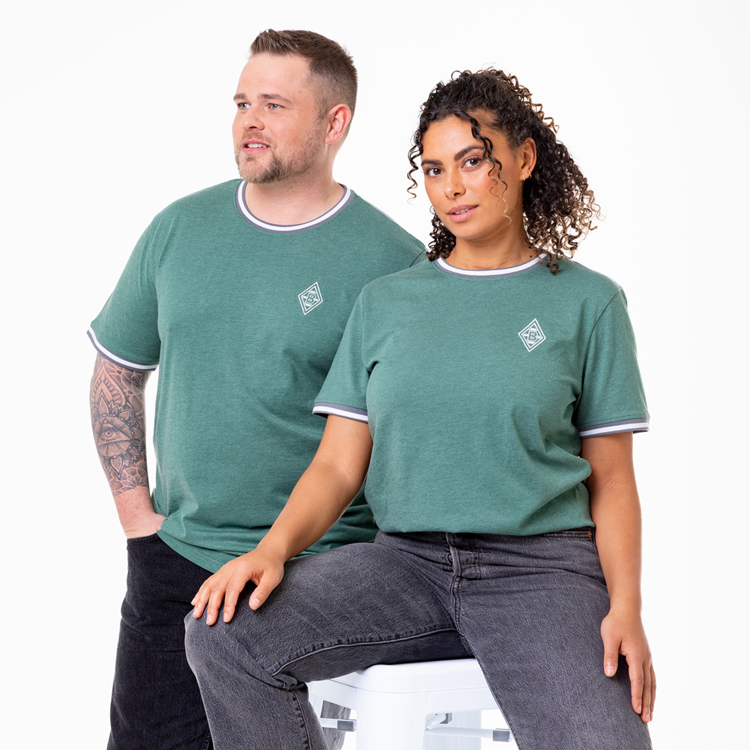Couple modeling green T-shirts with striped necklines sitting on a stool with the woman having curly hair.