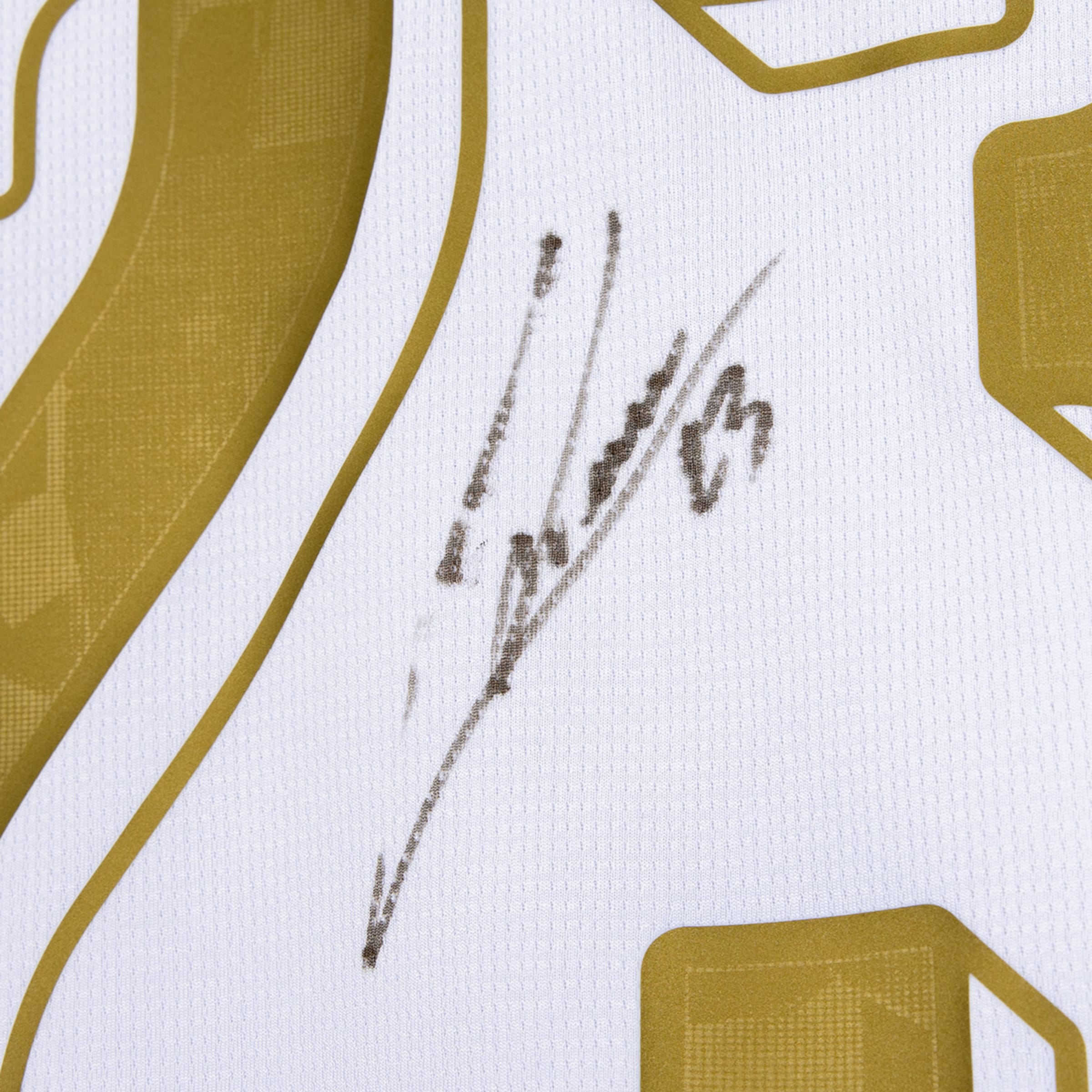 Nahaufnahme eines weißen Sporttrikots mit goldener Nummer und einem schwarzen Autogramm, das die Zahl 13 enthält.