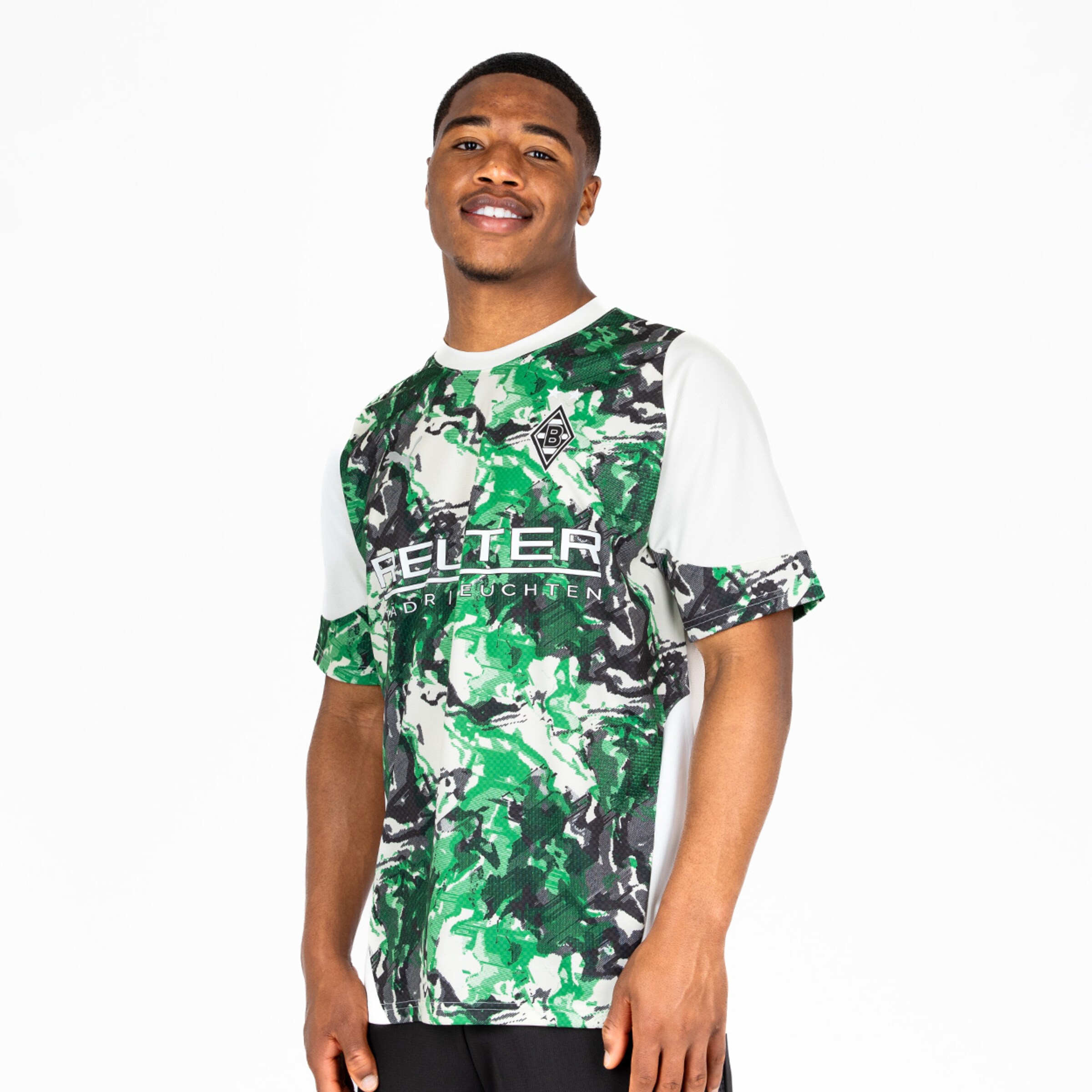 Junger Mann trägt ein künstlerisches Borussia Mönchengladbach Fußballtrikot in grün und schwarz. Er lächelt.