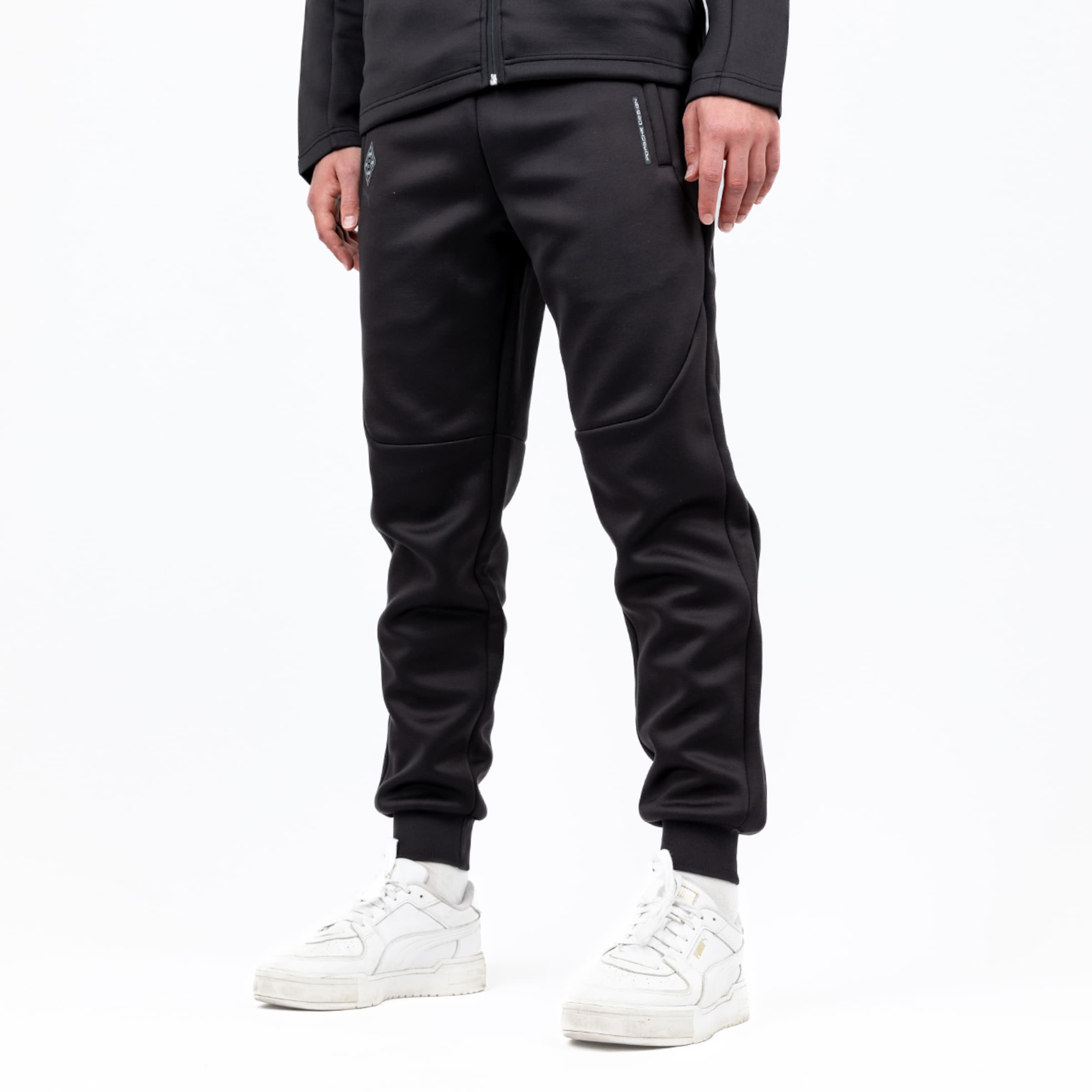 Schwarze Trainingshose mit elastischem Bund und seitlichen Taschen kombiniert mit weißen Sportschuhen.