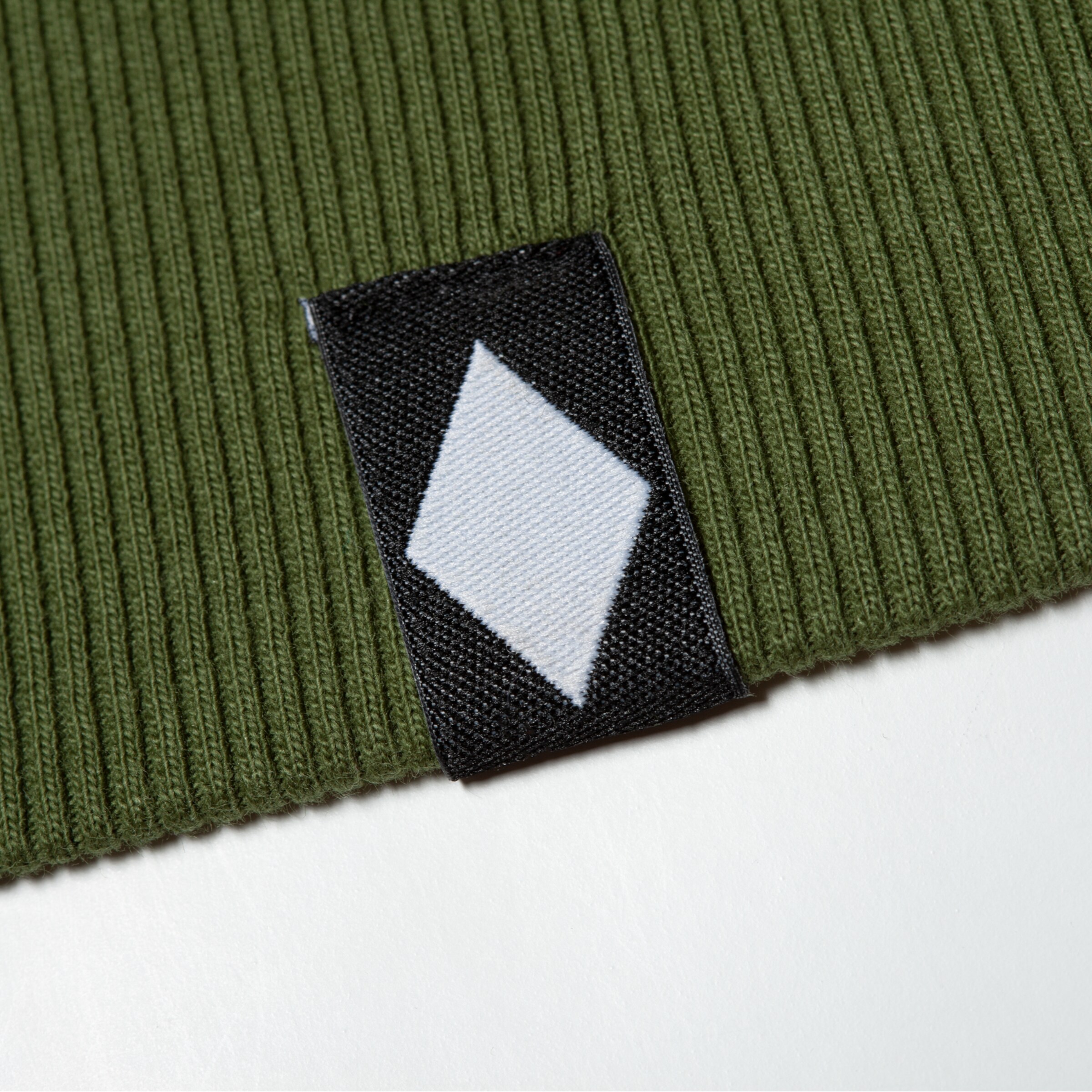 Ein schwarzes Etikett mit einem weißen Rauten-Symbol auf grünem geripptem Stoff.